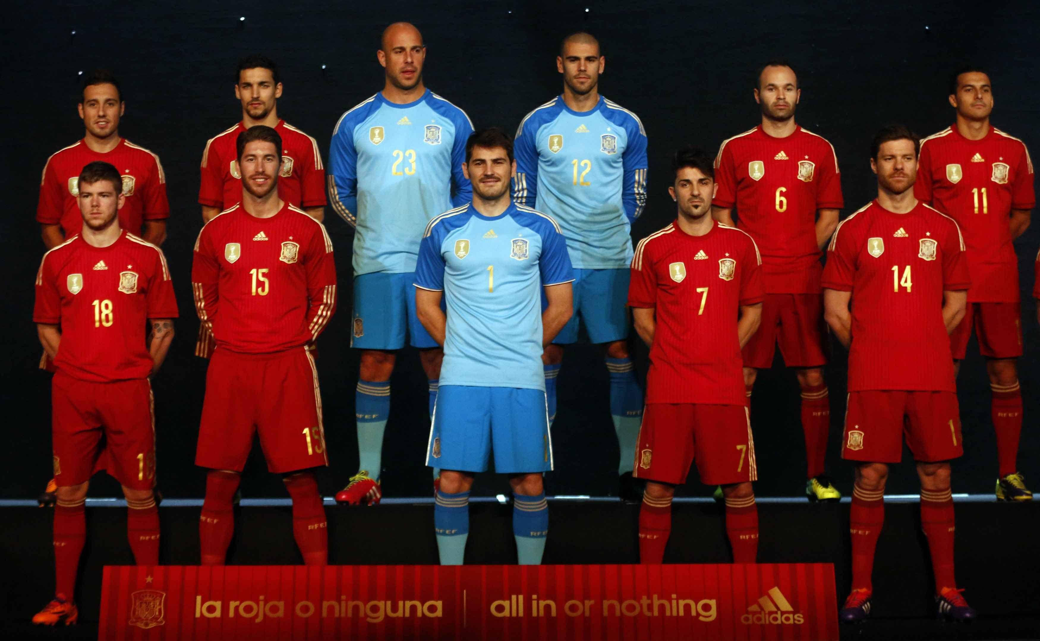 Spain 桌布 壁紙 — 西班牙國家足球隊球員身穿紅色和淺藍色球衣，在黑暗背景和發光地板文字前擺姿勢。