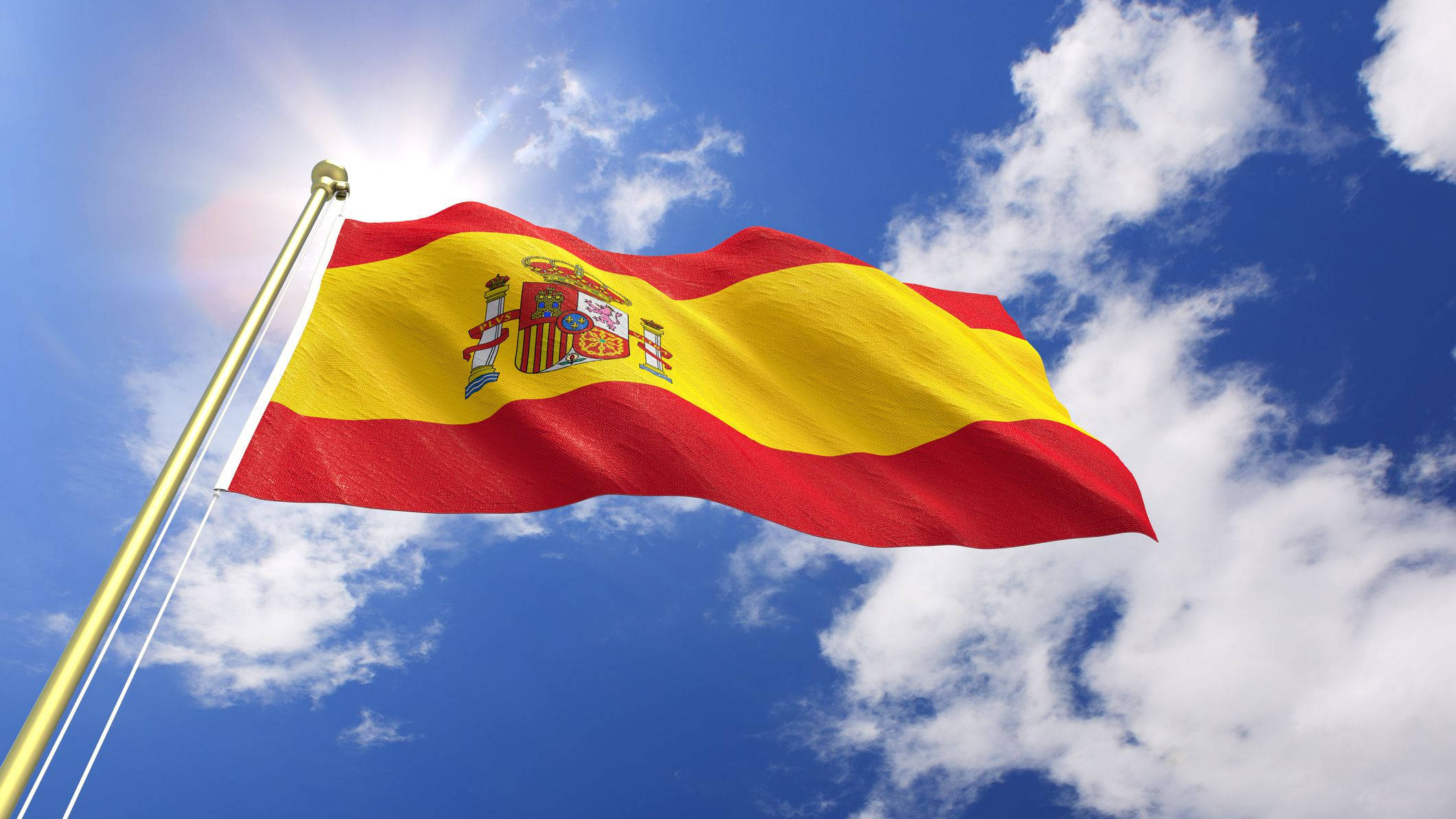 Spain Flag 桌布 壁紙 — 西班牙國旗在明亮的藍天、蓬鬆的白雲和陽光射線中自豪地飄揚。