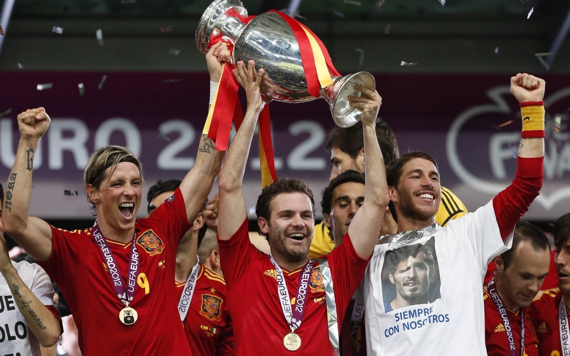 Spain 桌布 壁紙 — 西班牙足球運動員歡欣地高舉2012年歐洲國家盃獎盃，場內紙屑紛飛，充滿慶祝氣氛。