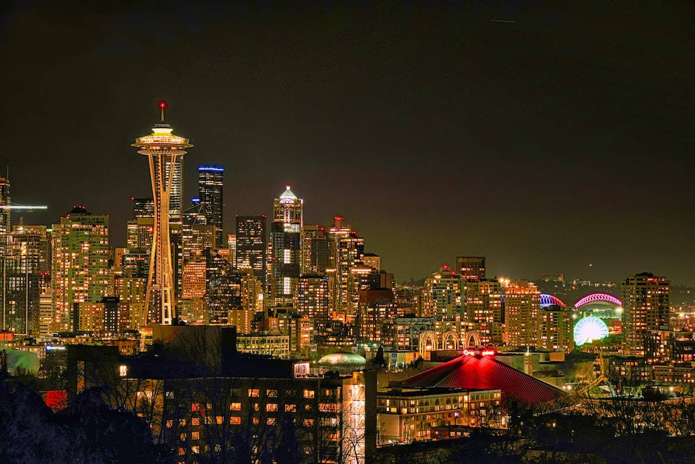 Seattle Skyline 桌布 壁紙 — 西雅圖夜晚天際線，太空針塔在黑暗天空中閃耀，城市燈光照亮建築物。