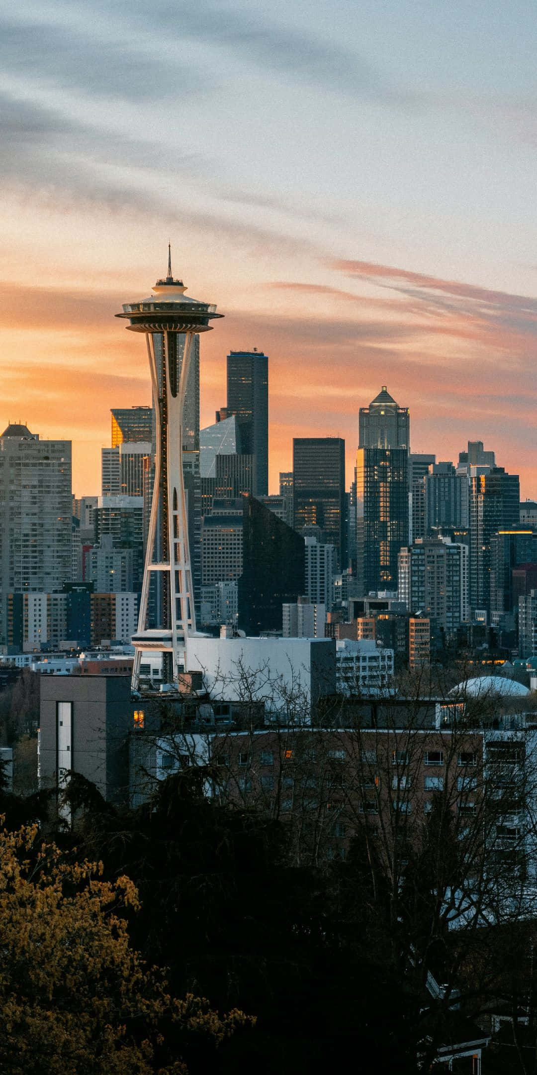 Pixel 3 Seattle 桌布 壁紙 — 西雅圖天際線在日落時分，太空針塔在橙色雲彩和前景剪影樹木的映襯下閃耀。