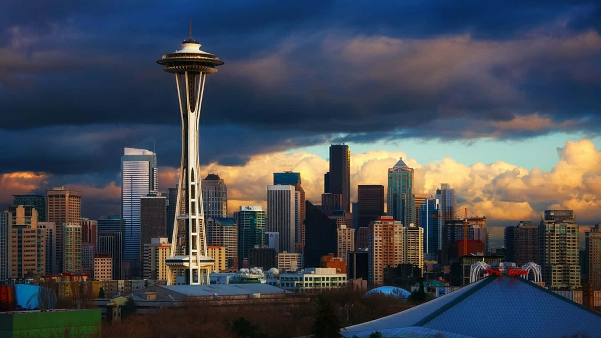 Seattle 桌布 壁紙 — 西雅圖天際線在日落時分，太空針塔在戲劇性的雲層下聳立於摩天大樓之上。