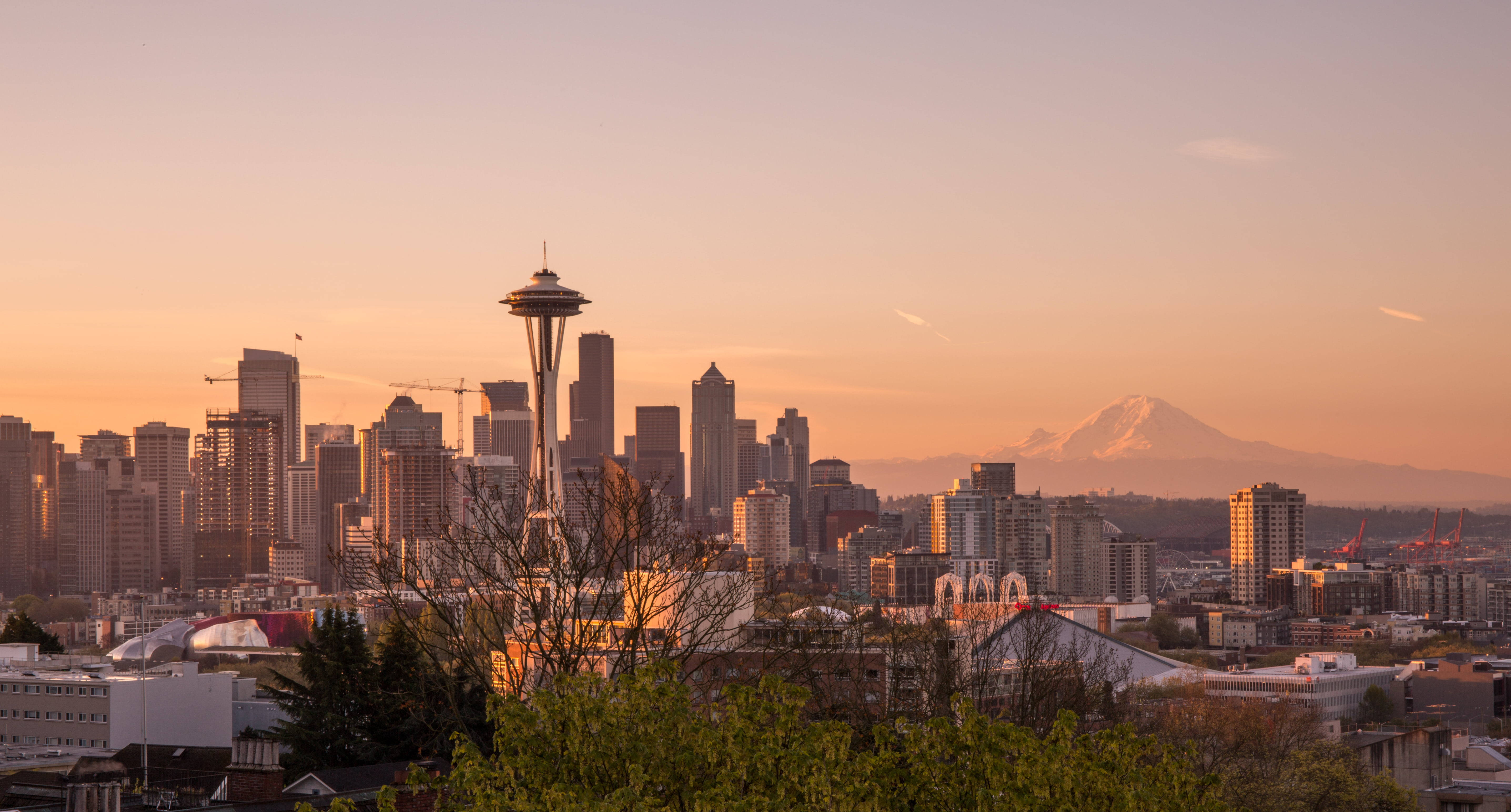 Space Needle 桌布 壁紙 — 西雅圖天際線在日落時分，太空針塔和積雪的雷尼爾山在溫暖的橙色光芒中閃耀。