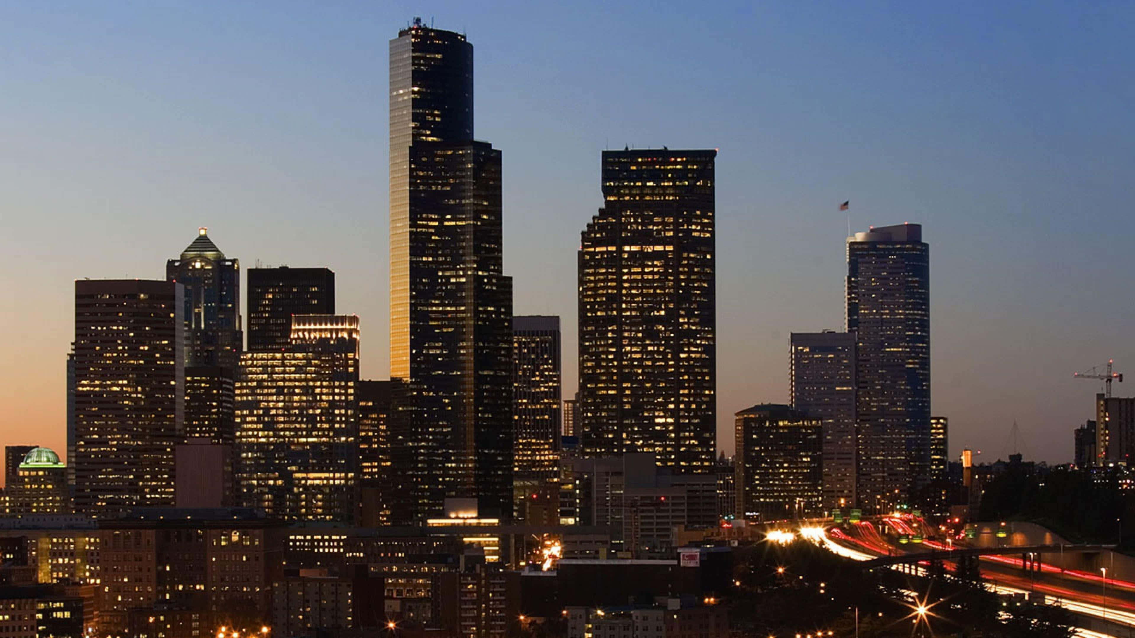 Seattle At Night 桌布 壁紙 — 西雅圖天際線在黃昏時分，亮燈的摩天大樓和下方發光的車流痕跡。