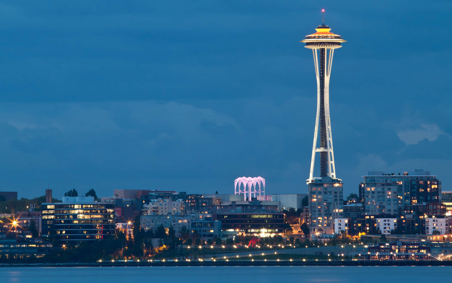Seattle At Night 桌布 壁紙 — 西雅圖天際線在黃昏時分，太空針塔在深藍色天空中閃耀，城市燈光倒映在水面上。