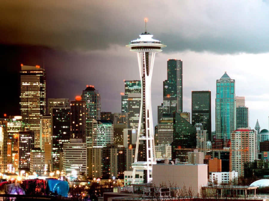 Seattle At Night 桌布 壁紙 — 西雅圖天際線在黃昏時分，太空針塔在暗雲和發光的摩天大樓映襯下亮起。