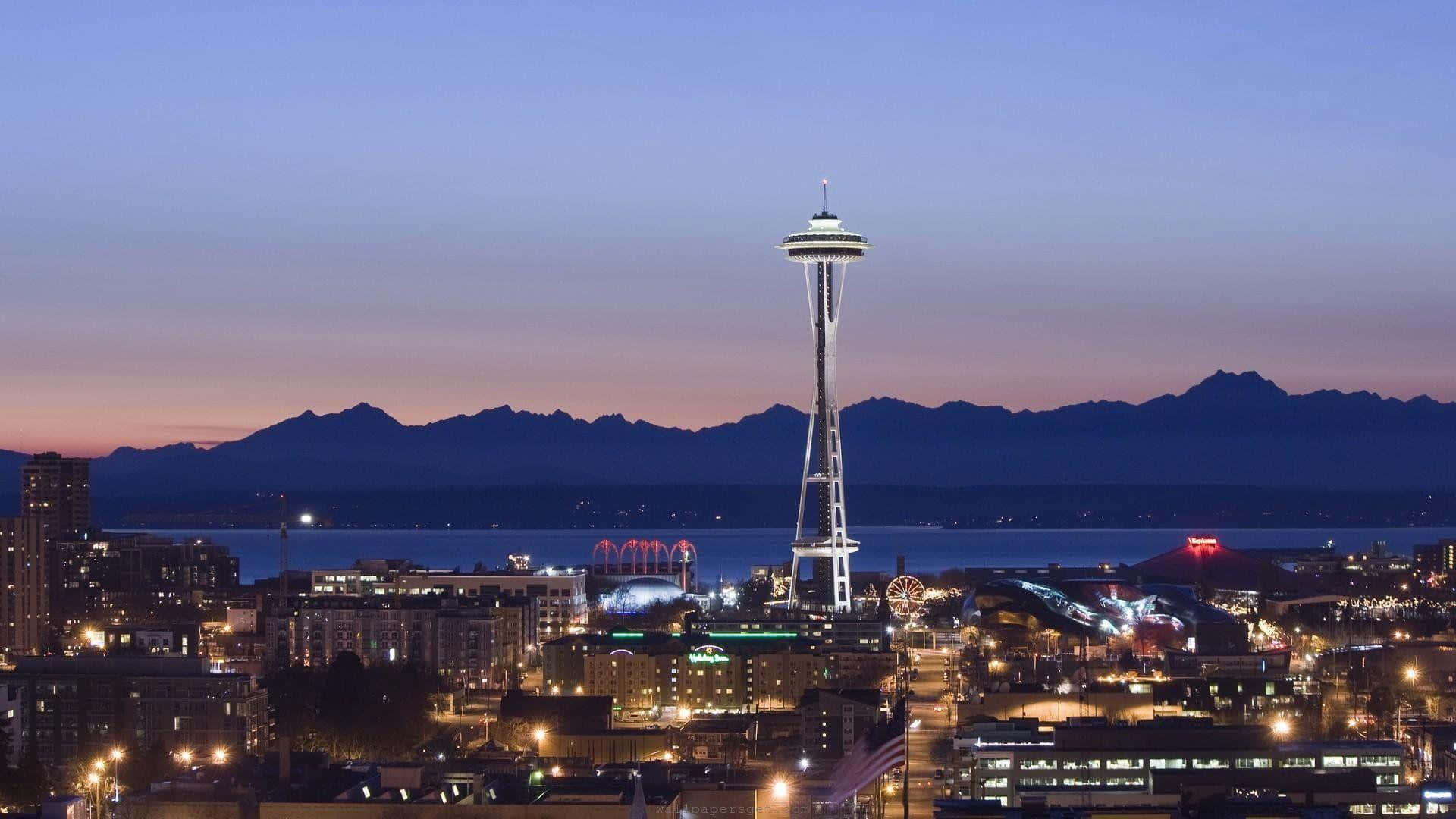 Seattle At Night 桌布 壁紙 — 西雅圖天際線在黃昏時分，太空針塔在紫色天空和遠山映襯下亮起燈光。