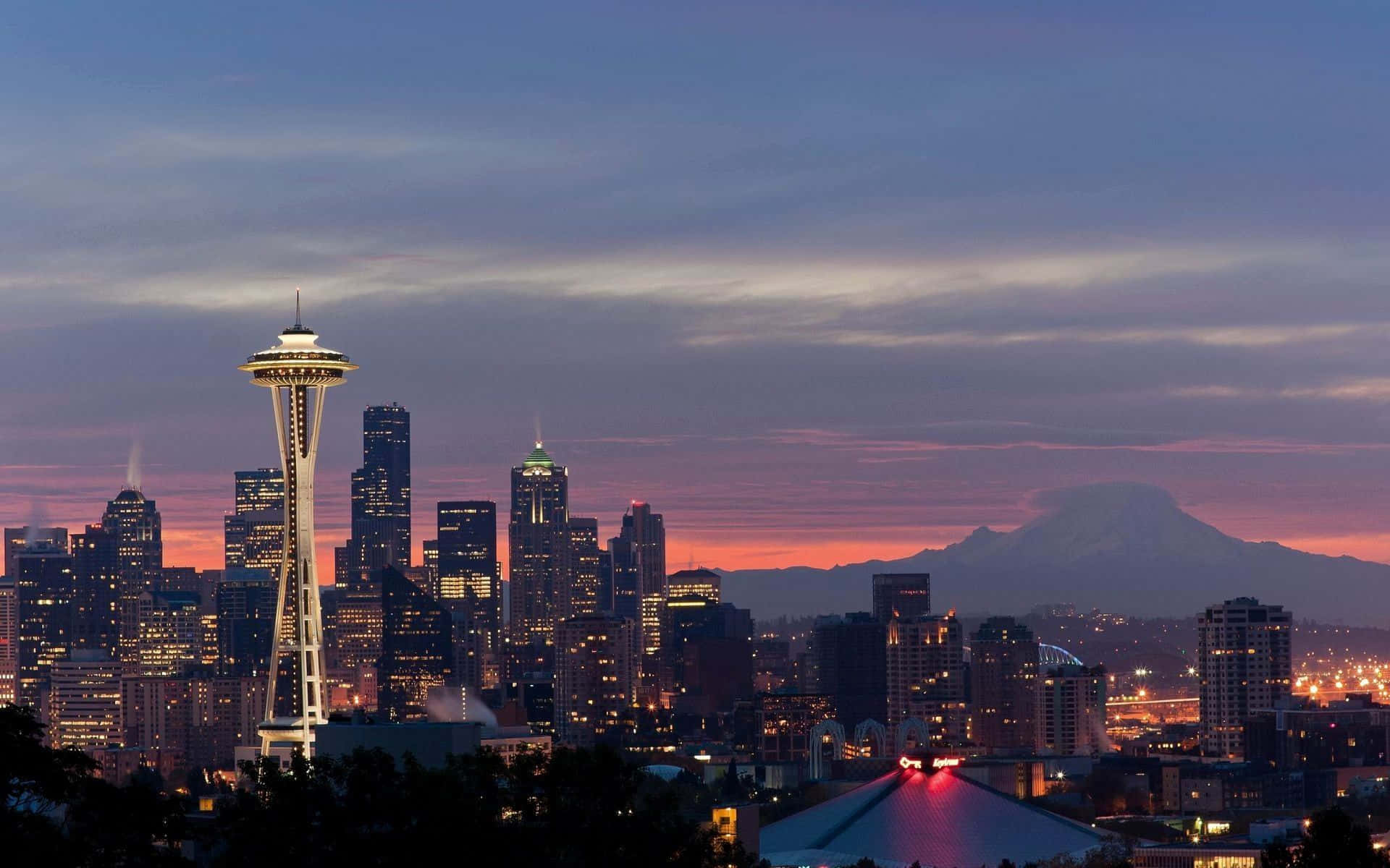 Seattle Washington 桌布 壁紙 — 西雅圖天際線在黃昏時分，太空針塔在紫橙色天空和遠處積雪覆蓋的山峰映襯下閃耀。