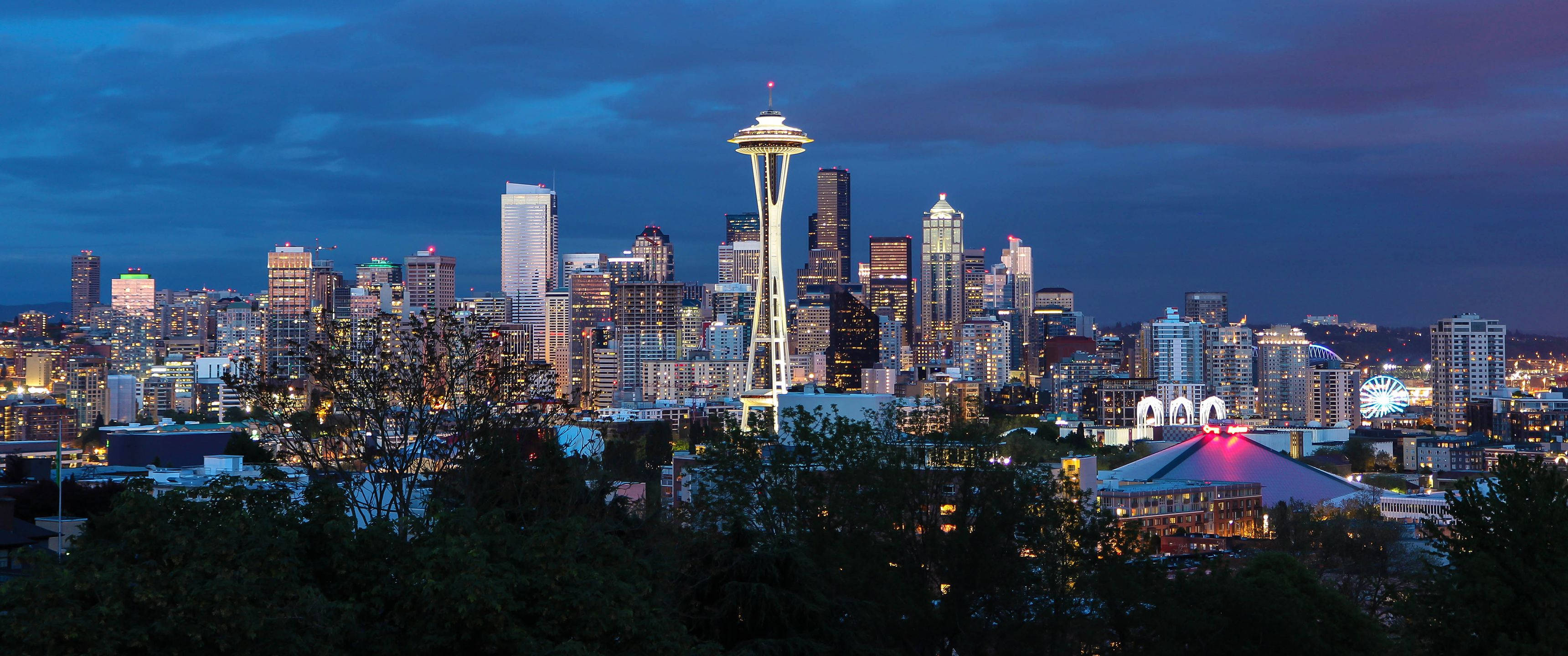 Seattle 桌布 壁紙 — 西雅圖天際線在黃昏時分，太空針塔在深藍色天空下亮起，城市燈光在下方閃爍。