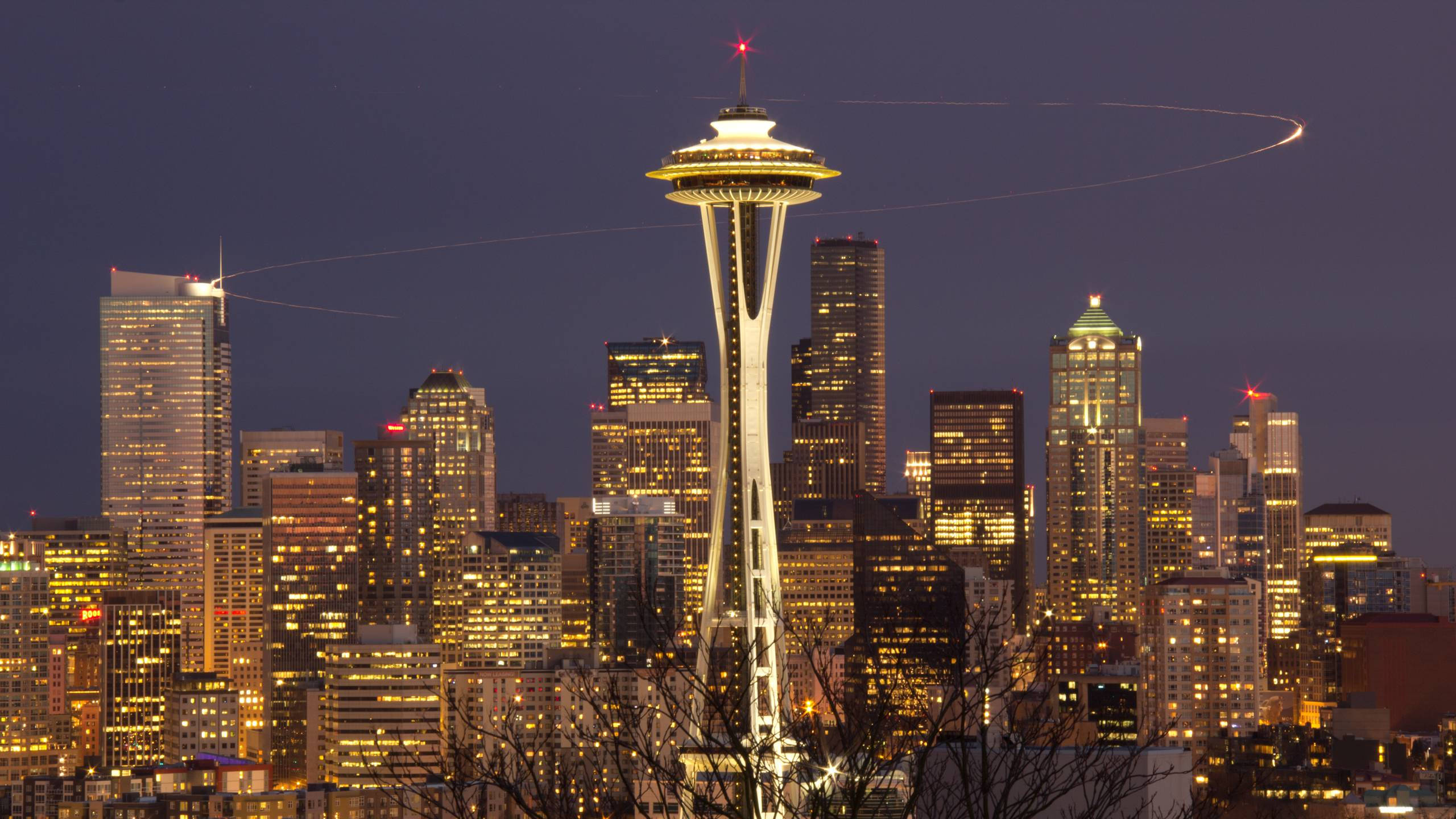 Space Needle 桌布 壁紙 — 西雅圖天際線在黃昏時分，太空針塔亮起燈光，飛機尾跡在紫色天空中劃出弧線。