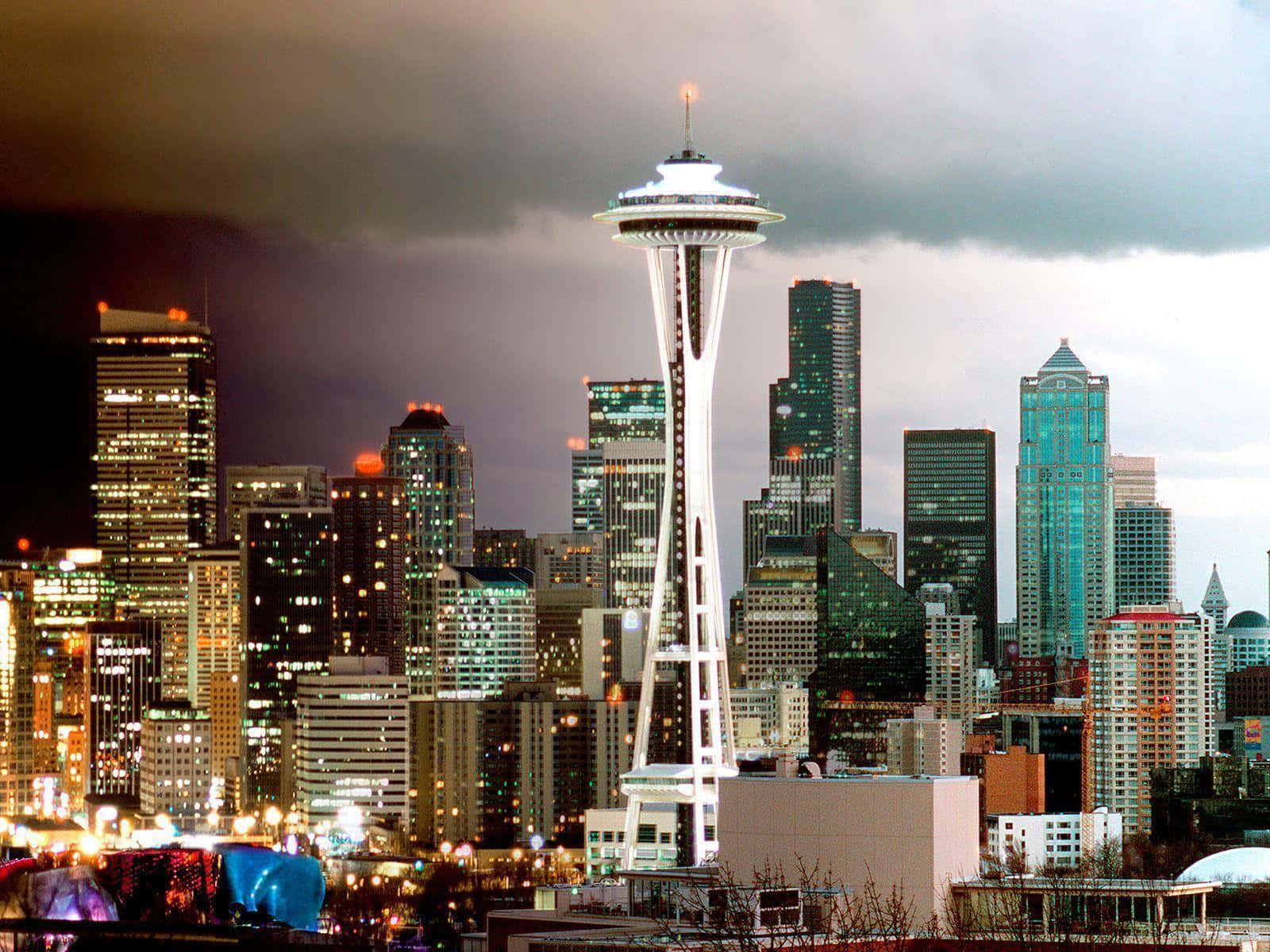 Seattle At Night 桌布 壁紙 — 西雅圖天際線在黃昏時分，太空針塔在烏雲和城市燈光中閃耀。