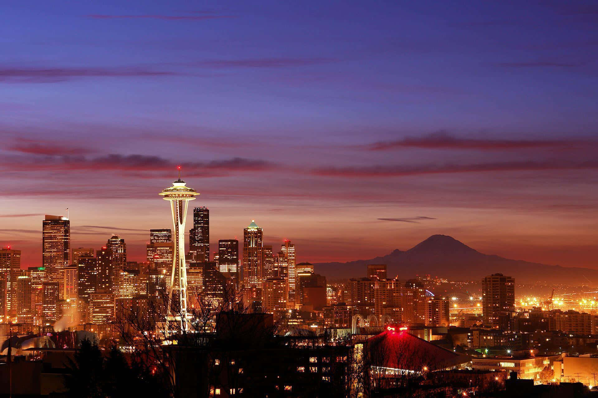 Seattle At Night 桌布 壁紙 — 西雅圖天際線在黃昏時分，太空針塔在紫色和橙色的天空下亮起，遠處可見雷尼爾山。