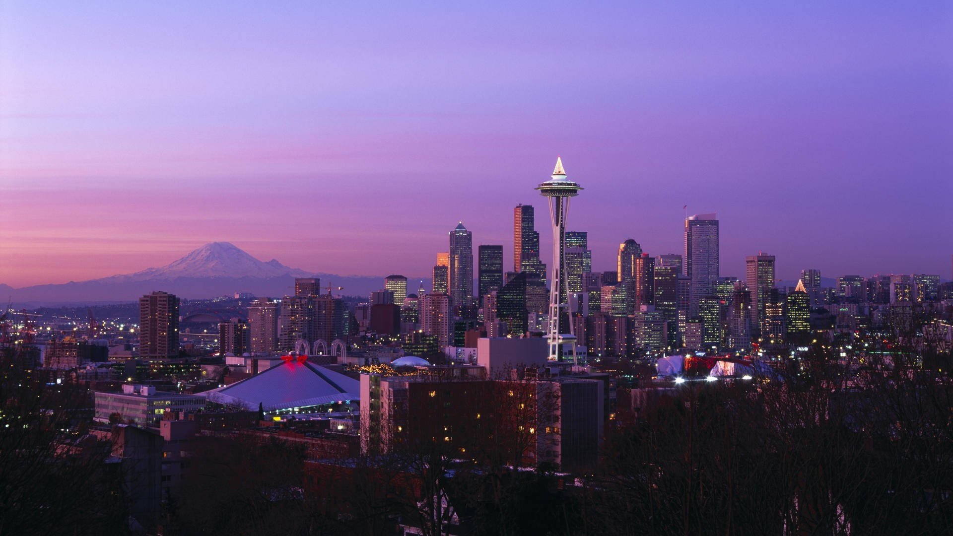 Seattle Skyline 桌布 壁紙 — 西雅圖天際線在黃昏時分，太空針塔亮起，雷尼爾山在紫色天空下遠方發光。