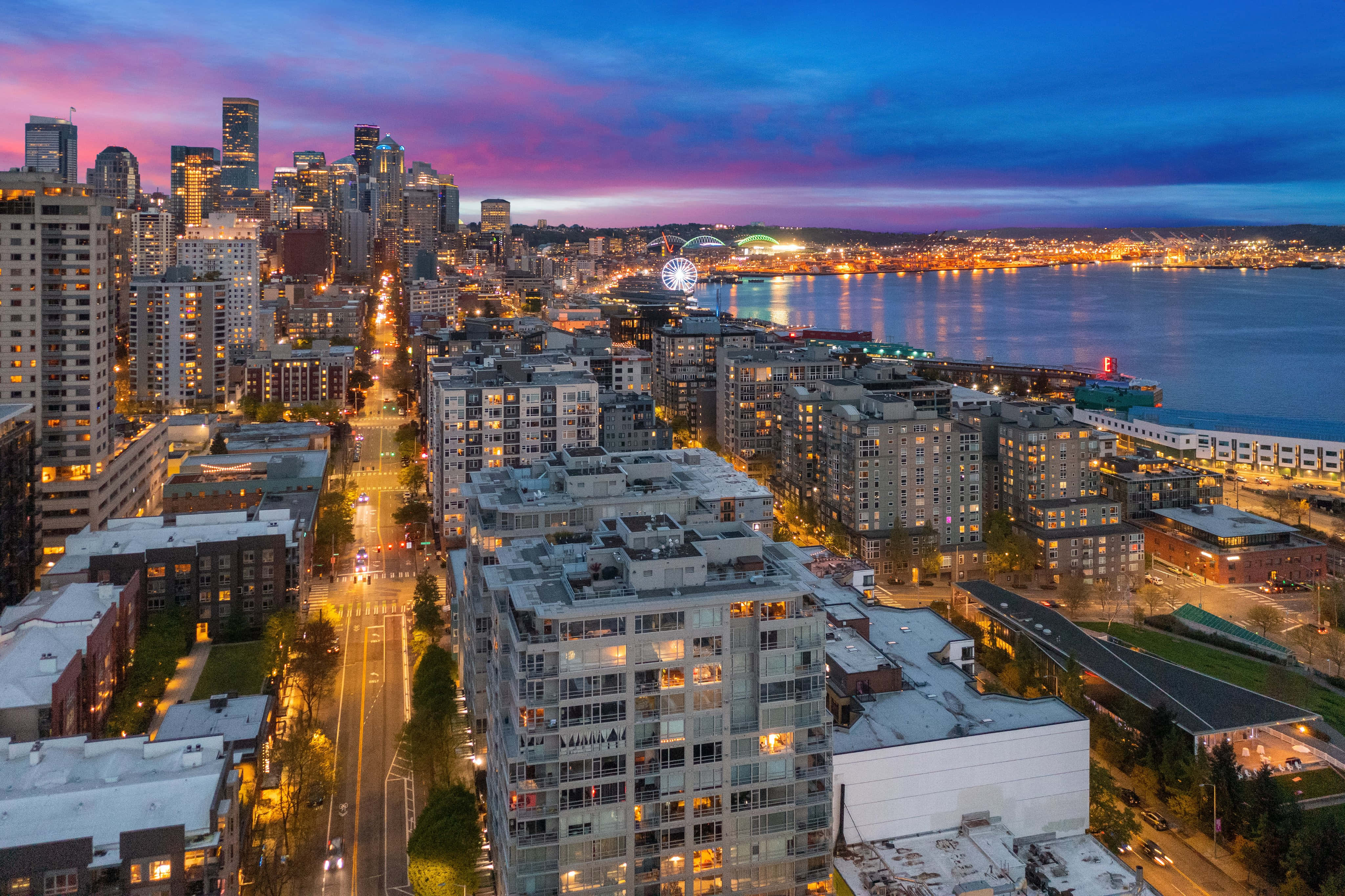 washington state 桌布 壁紙 — 西雅圖天際線在黃昏時的鳥瞰圖，城市燈光閃爍，倒映在水面上，天空呈現鮮豔的紫藍色。