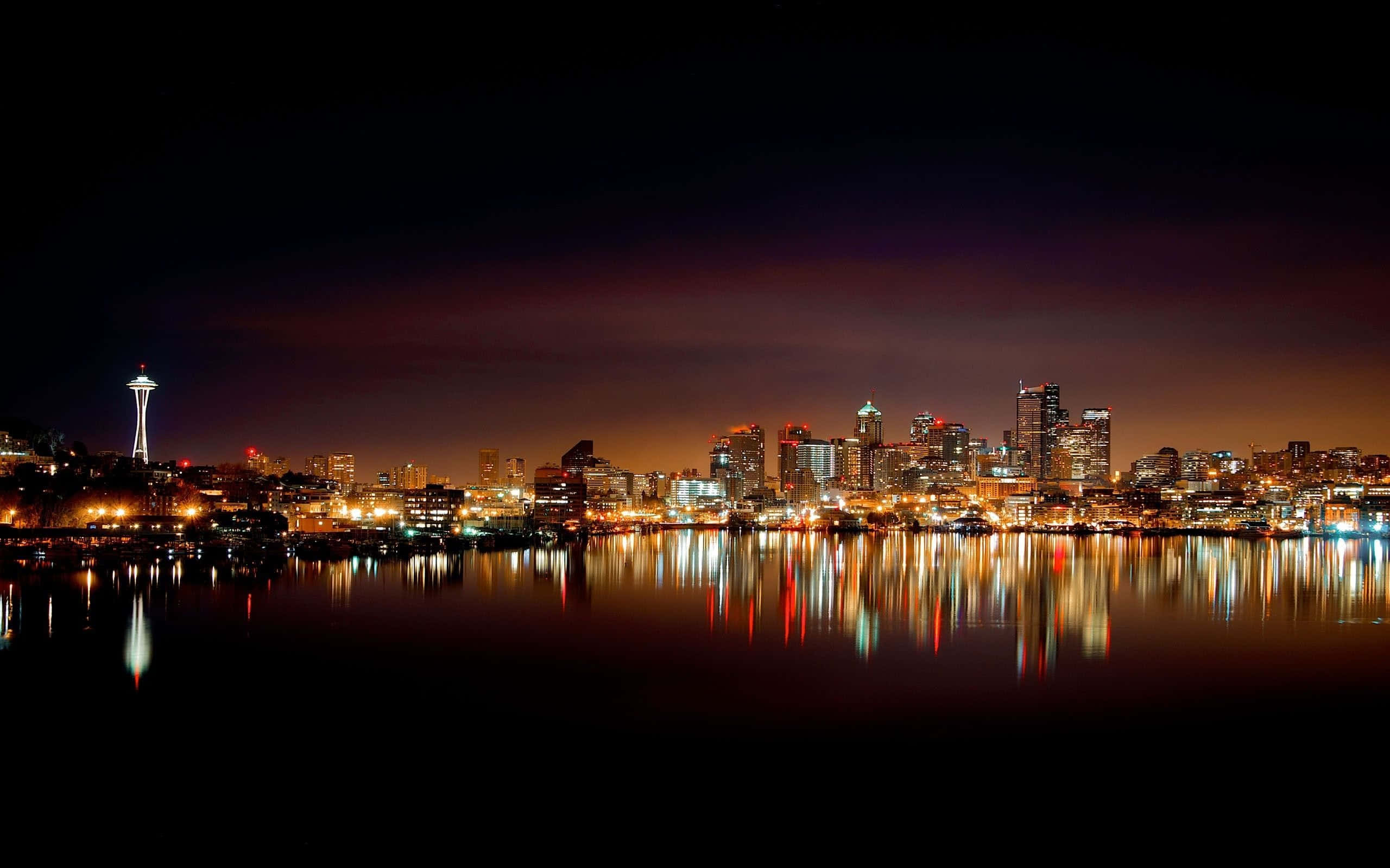 水 桌布 壁紙 — 西雅圖天際線夜景，太空針塔亮起，城市燈光在平靜的水面上倒映，天空漆黑。