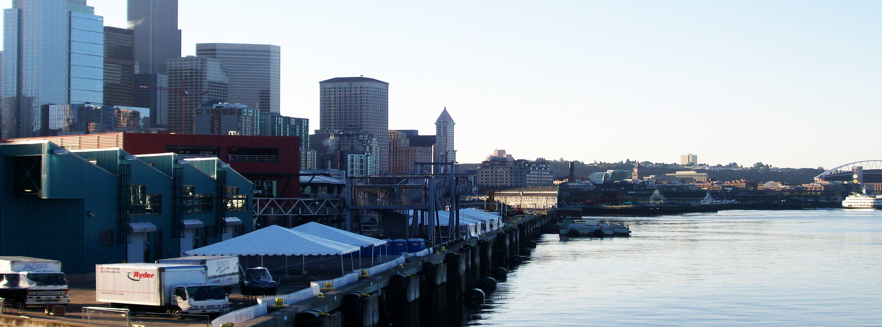 西雅圖 桌布 壁紙 — 西雅圖天際線的明亮日間景觀，現代摩天大樓和延伸至平靜水面的長碼頭。