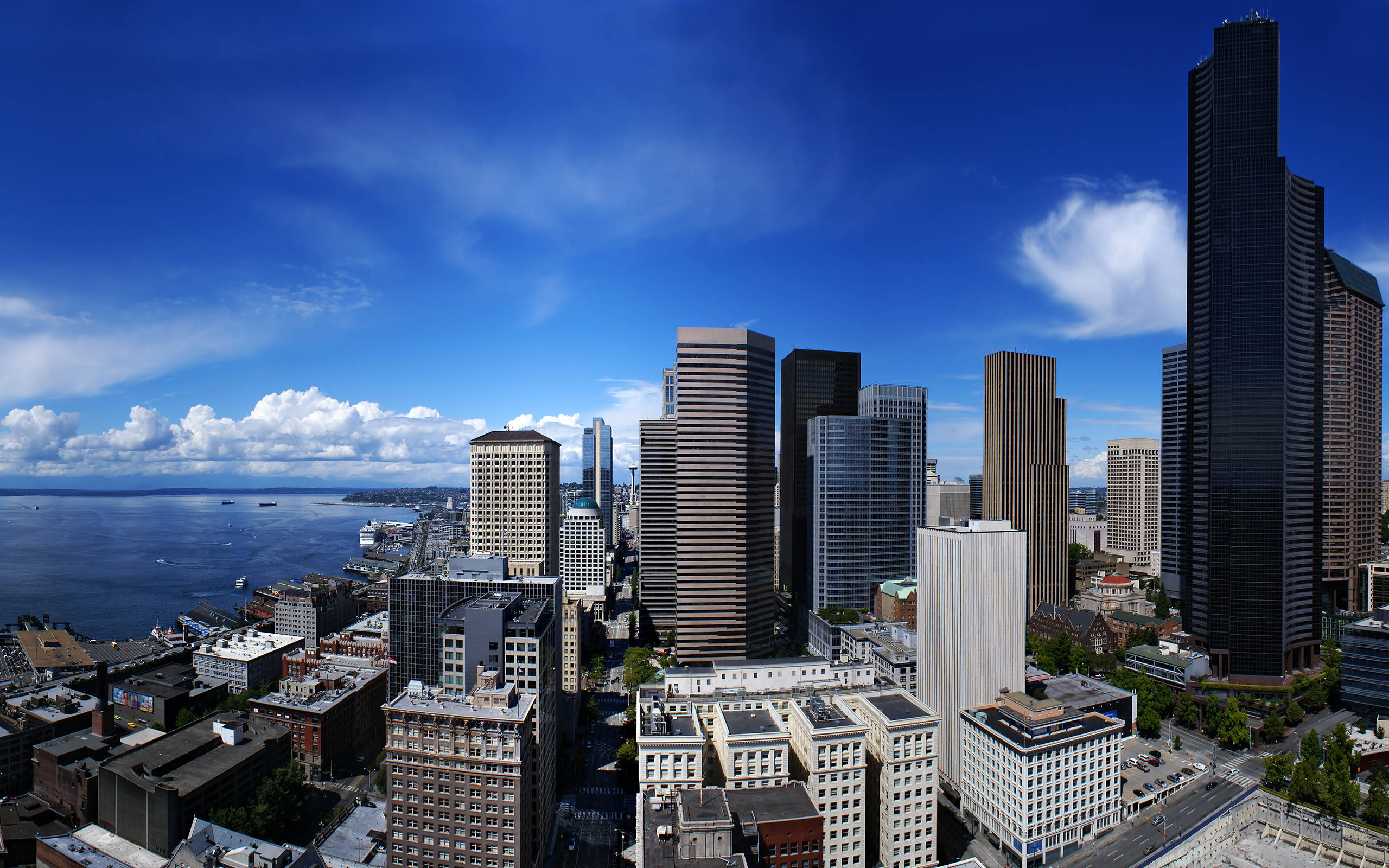 Seattle 桌布 壁紙 — 西雅圖天際線的鳥瞰圖，包括太空針塔和海濱，在晴朗藍天和蓬鬆白雲下。