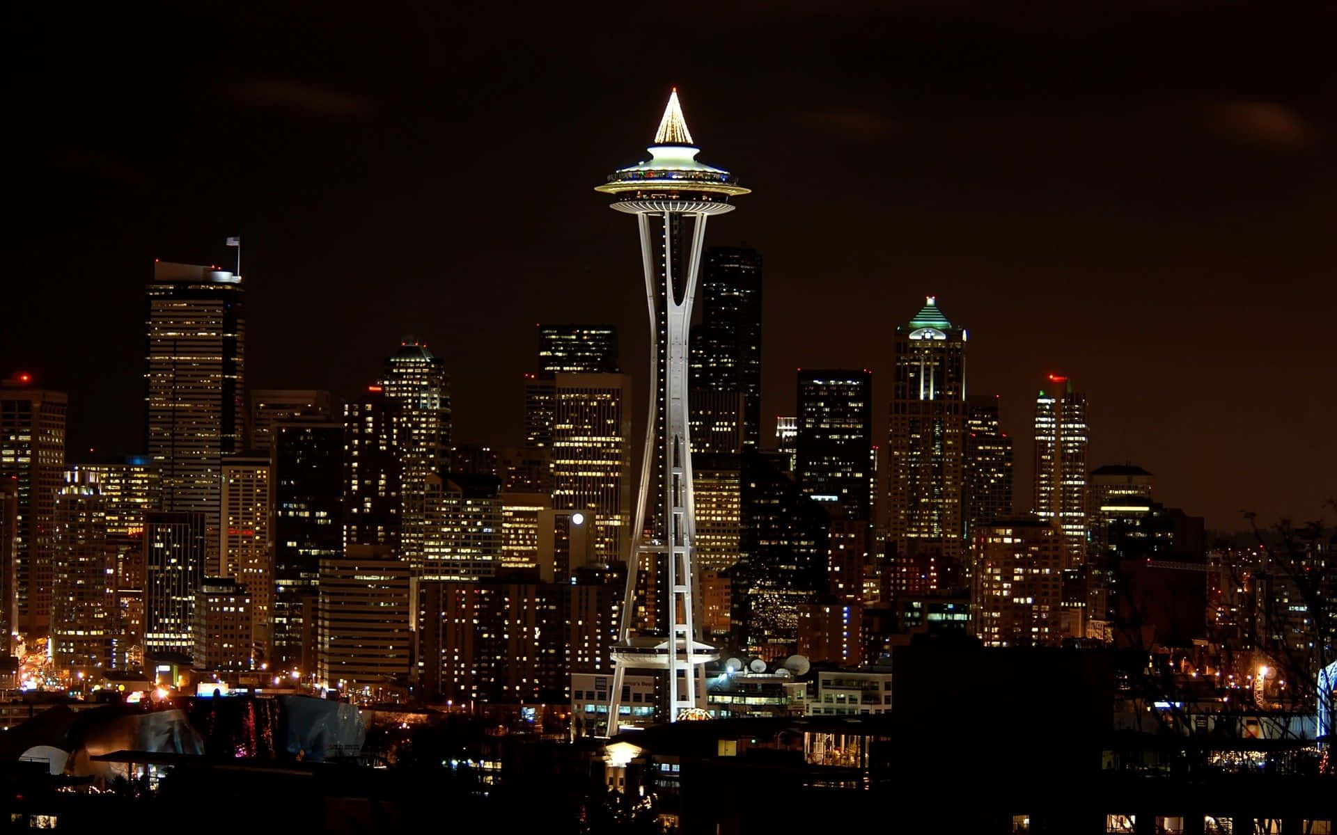 Seattle At Night 桌布 壁紙 — 西雅圖標誌性的太空針塔在漆黑的夜空中閃耀，周圍是充滿活力的城市天際線，高樓大廈燈火通明。