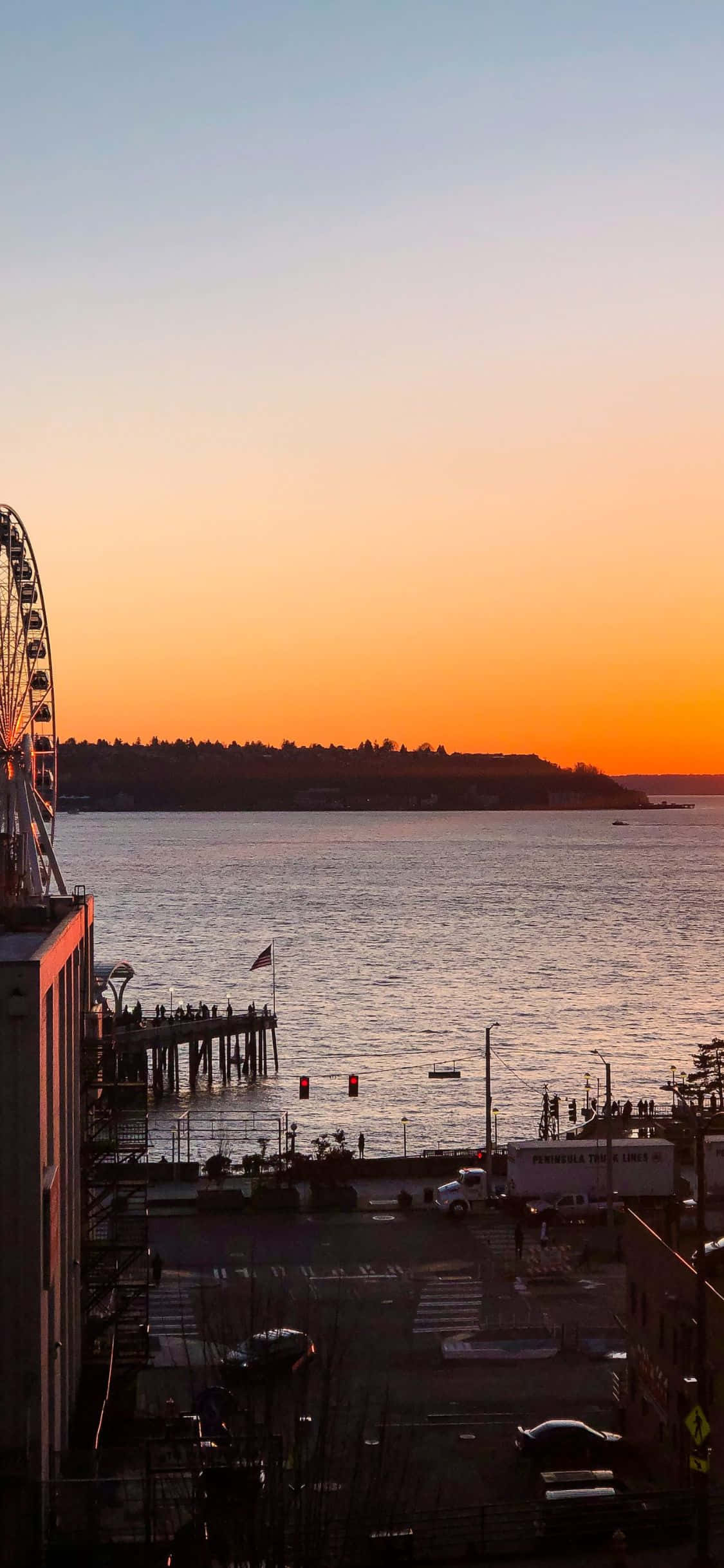 iPhone X Seattle 桌布 壁紙 — 西雅圖海濱的 vibrant 日落，摩天輪在橙色和藍色天空的襯托下呈現剪影。