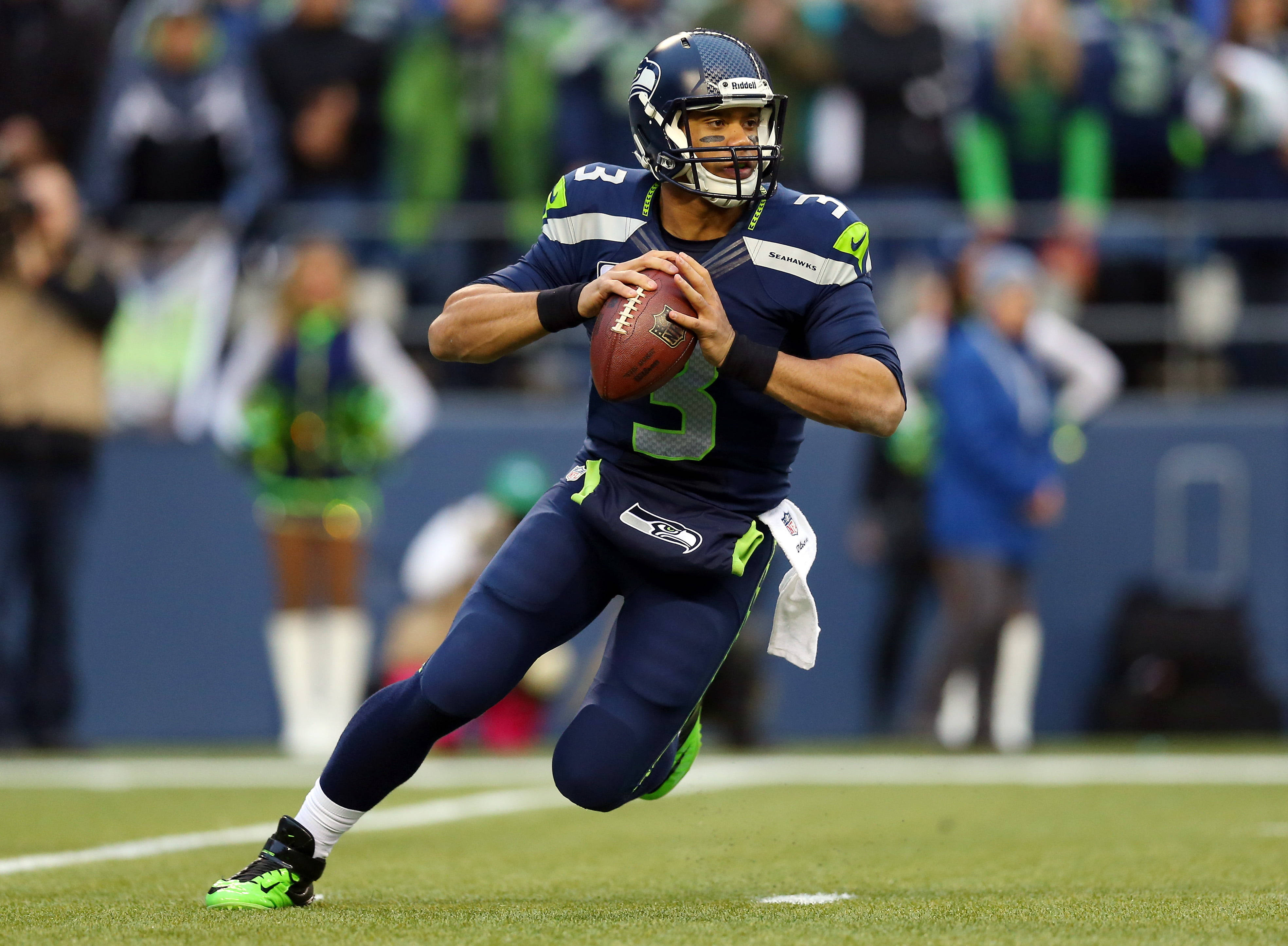 Seattle Seahawks 桌布 壁紙 — 西雅圖海鷹隊四分衛拉塞爾·威爾遜身穿海軍藍制服，在綠色球場上準備擲出橄欖球。