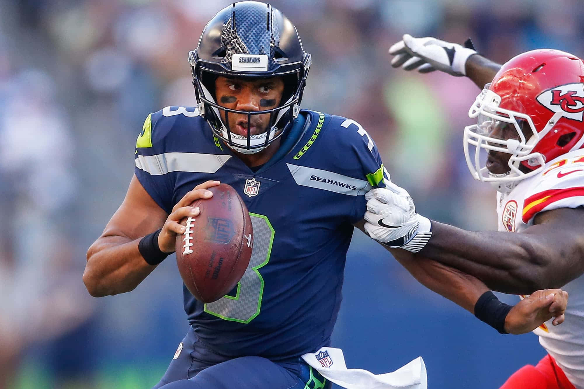 NFL 桌布 壁紙 — 西雅圖海鷹隊四分衛羅素·威爾遜持球衝刺，堪薩斯城酋長隊防守球員在激烈的NFL比賽中逼近。