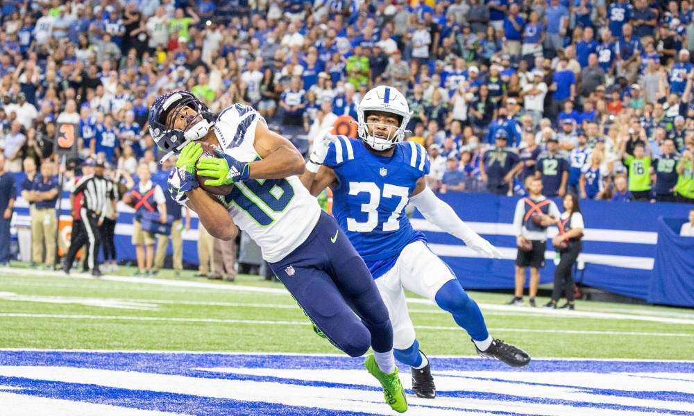 Seattle Seahawks 桌布 壁紙 — 西雅圖海鷹隊的白藍色接球手跳起接住美式足球，而印第安納波利斯小馬隊的藍色防守球員在座無虛席的球場比賽中逼近。