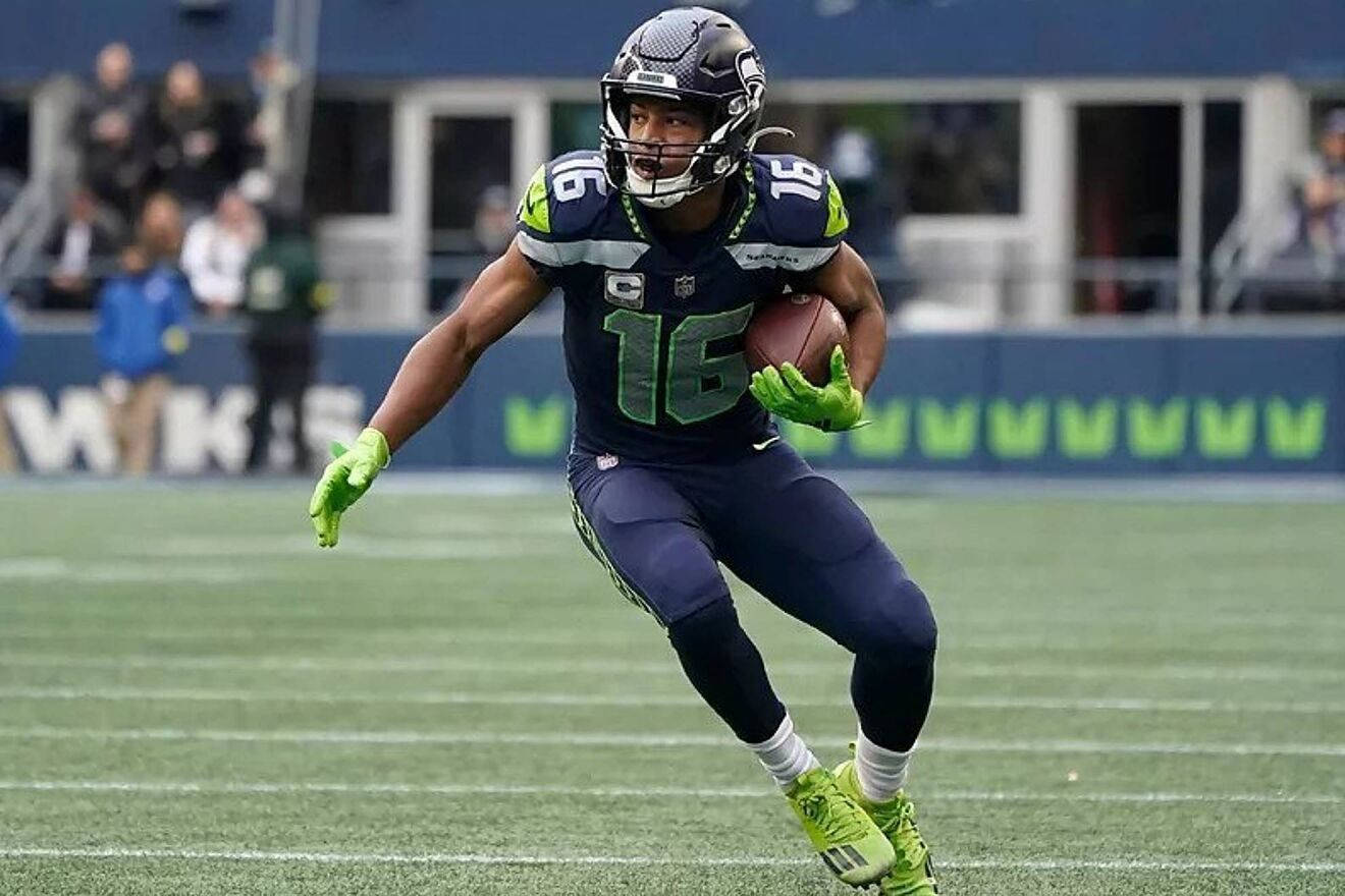 Seattle Seahawks 桌布 壁紙 — 西雅圖海鷹隊的美式足球員身穿海軍藍和螢光綠色裝備，抱著球衝過球場。