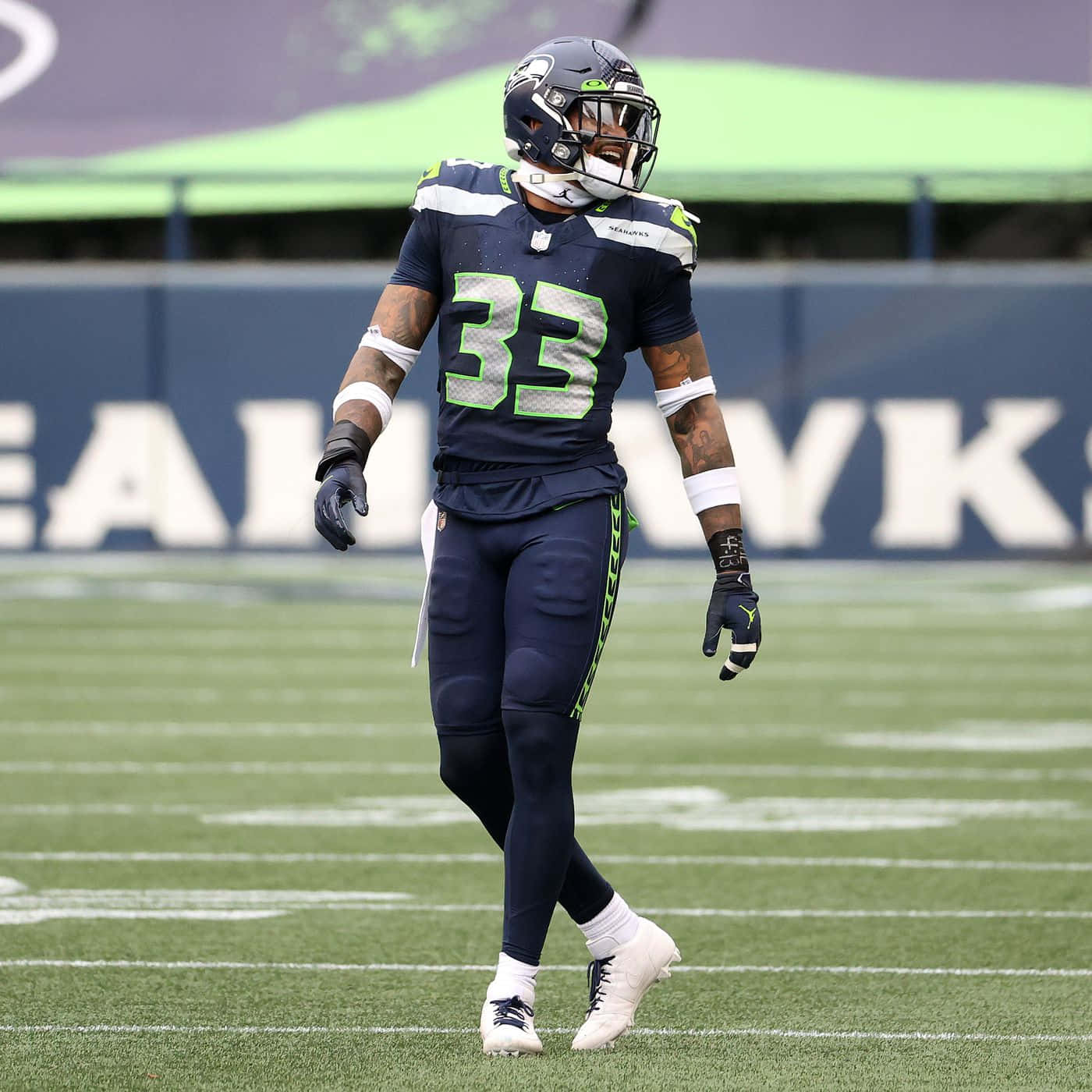 Seattle Seahawks 桌布 壁紙 — 西雅圖海鷹隊美式足球員33號在比賽期間穿著全套裝備在綠色場地上行走。