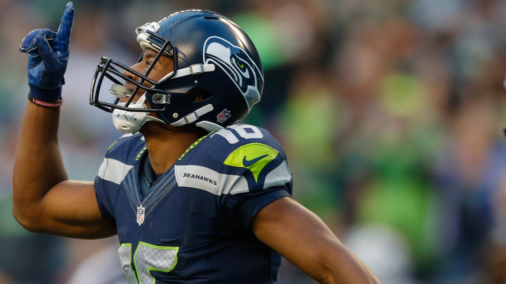 Seattle Seahawks 桌布 壁紙 — 西雅圖海鷹隊美式足球員身穿藍綠球衣，比賽中舉起戴手套的手指作出勝利姿勢。