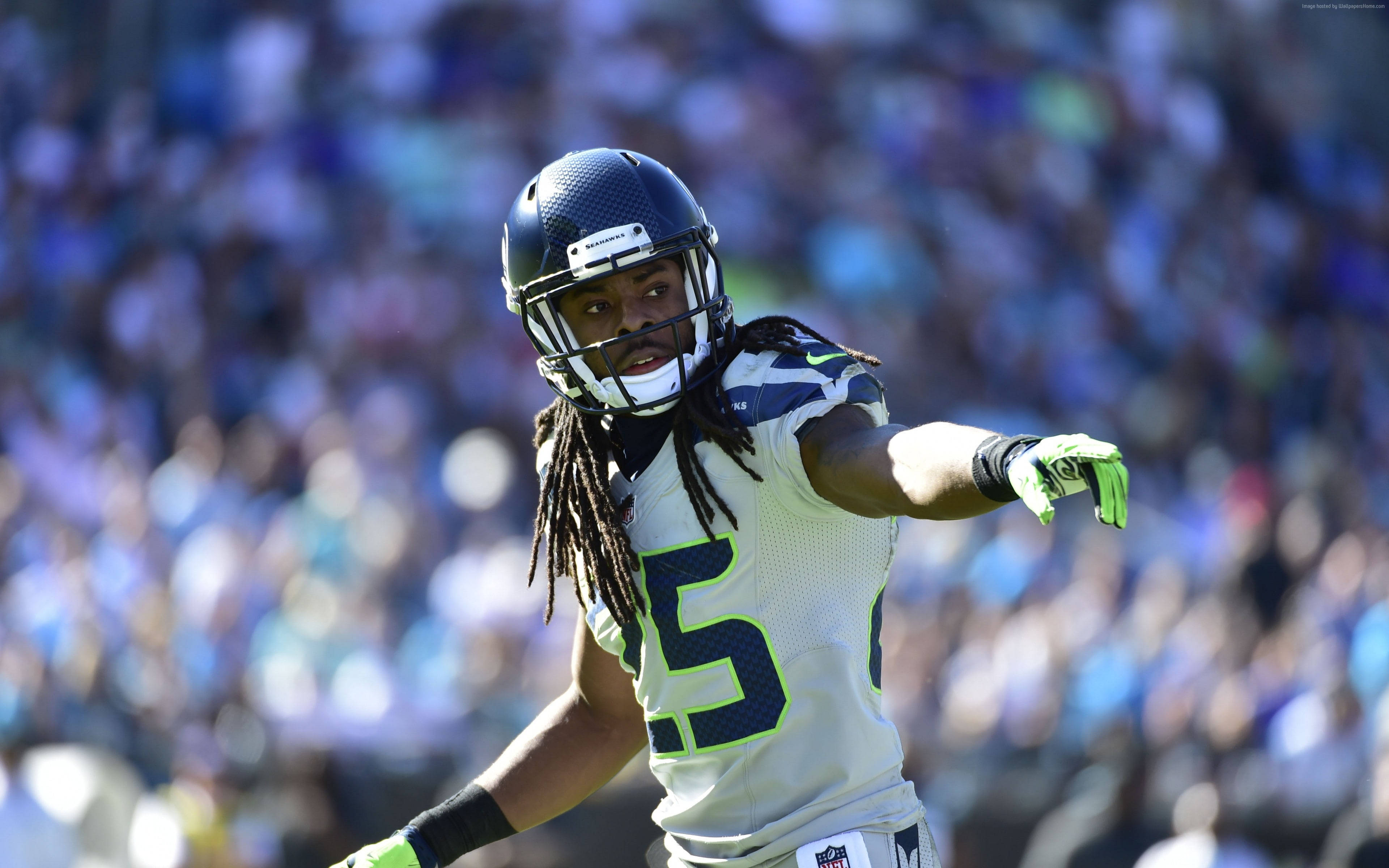 Seattle Seahawks 桌布 壁紙 — 西雅圖海鷹隊美式足球運動員在陽光明媚的日子裡行動，背景是模糊的人群。