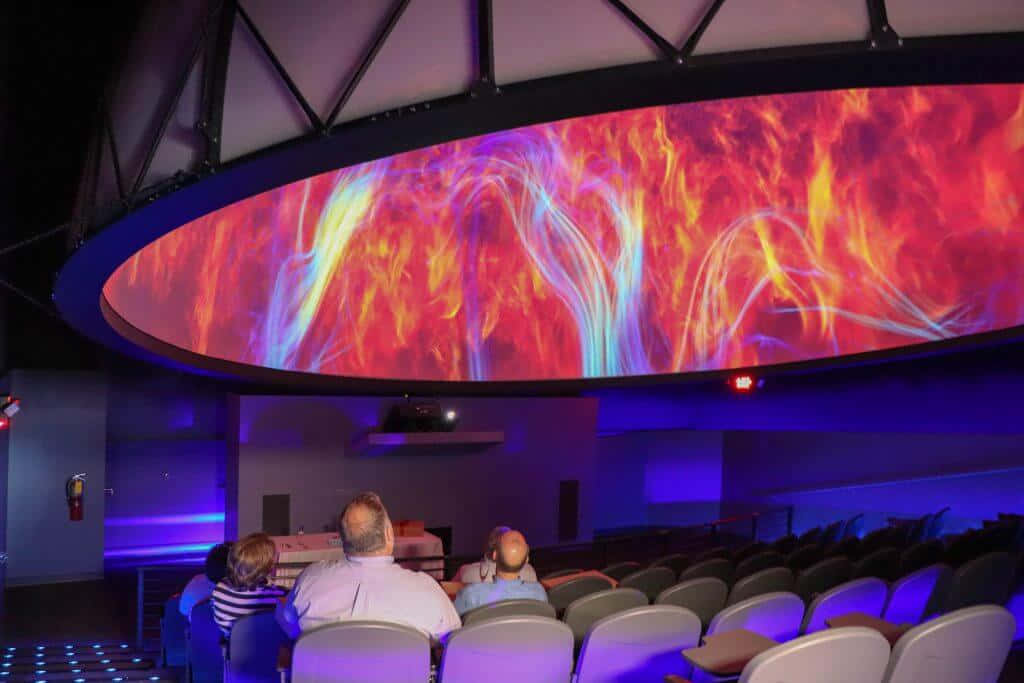 Planetarium 桌布 壁紙 — 觀眾在漆黑的影院中觀看弧形穹頂螢幕上充滿活力的宇宙火焰表演。
