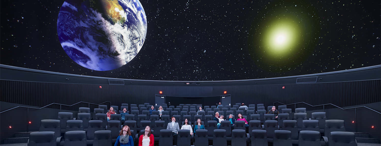 Planetarium 桌布 壁紙 — 觀眾在黑暗的沉浸式圓頂劇院觀看地球和一顆發光恆星的宇宙投影。