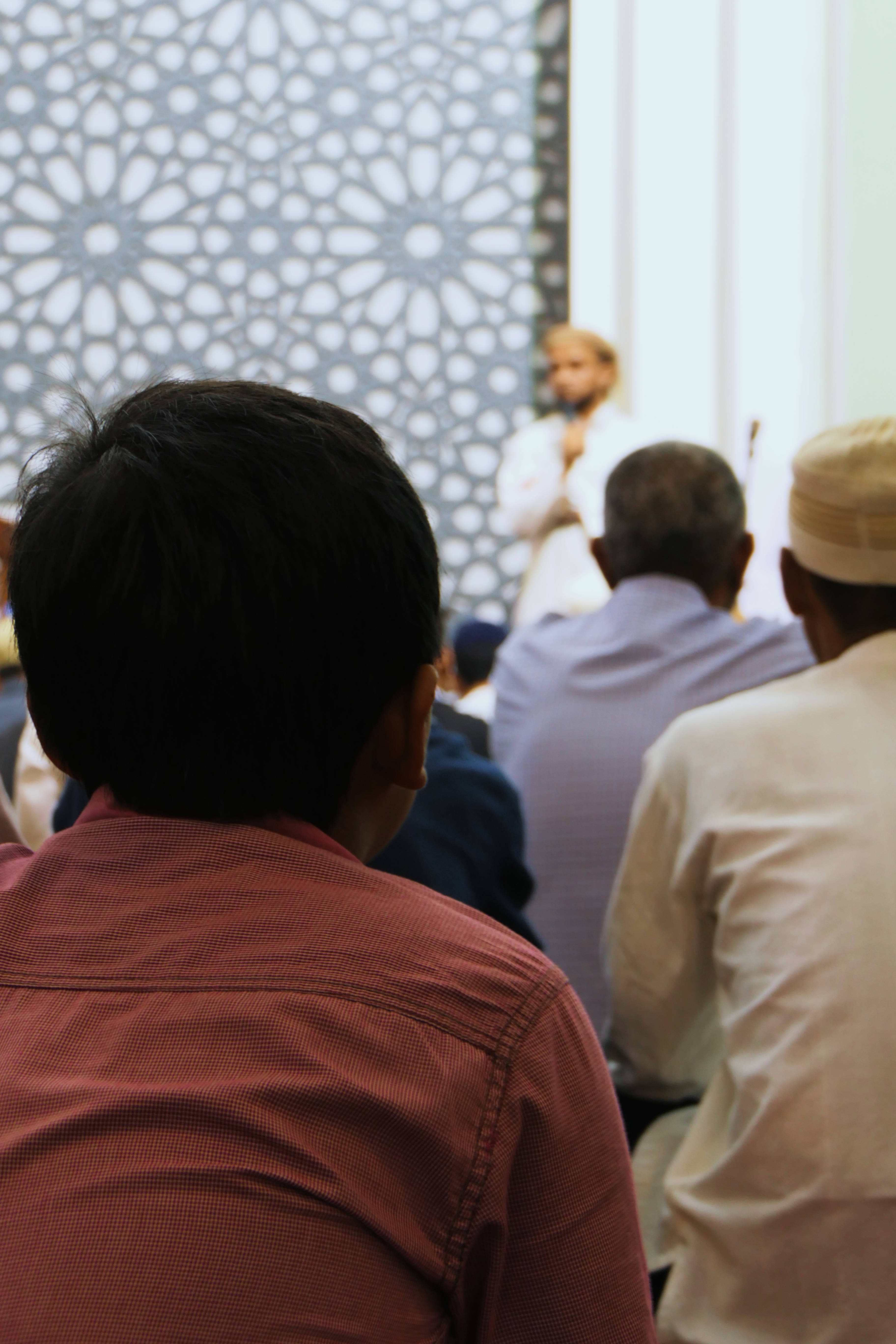 Ramadan 桌布 壁紙 — 觀眾坐在一個光線柔和的室內空間，面向一個精緻幾何螢幕後面的演講者。