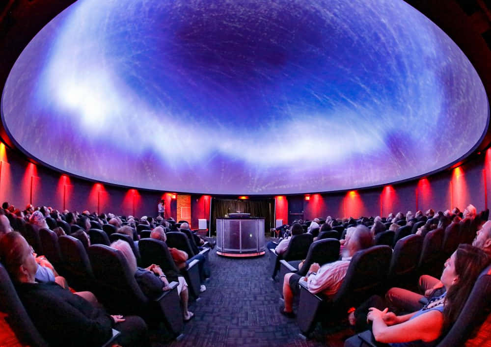 Planetarium 桌布 壁紙 — 觀眾坐在天文館內，觀看弧形圓頂天花板上的宇宙投影。