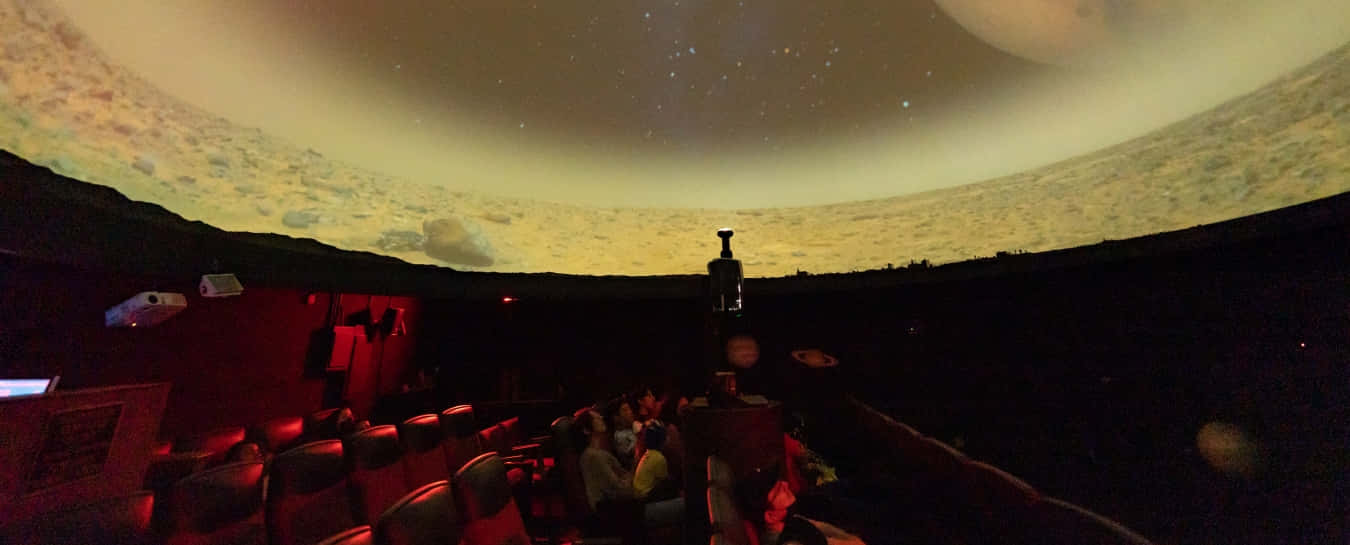 Planetarium 桌布 壁紙 — 觀眾坐在黑暗的天文館中，觀看星空和外星行星的生動投影。