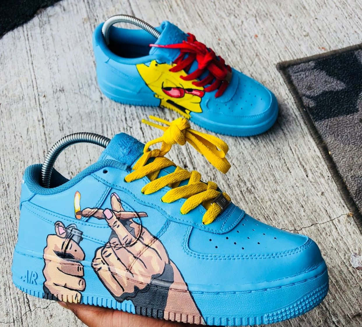 Nike Air Force 桌布 壁紙 — 訂製藍色運動鞋，鞋帶上有卡通手點燃香煙和辛普森面孔，放在風化木上。