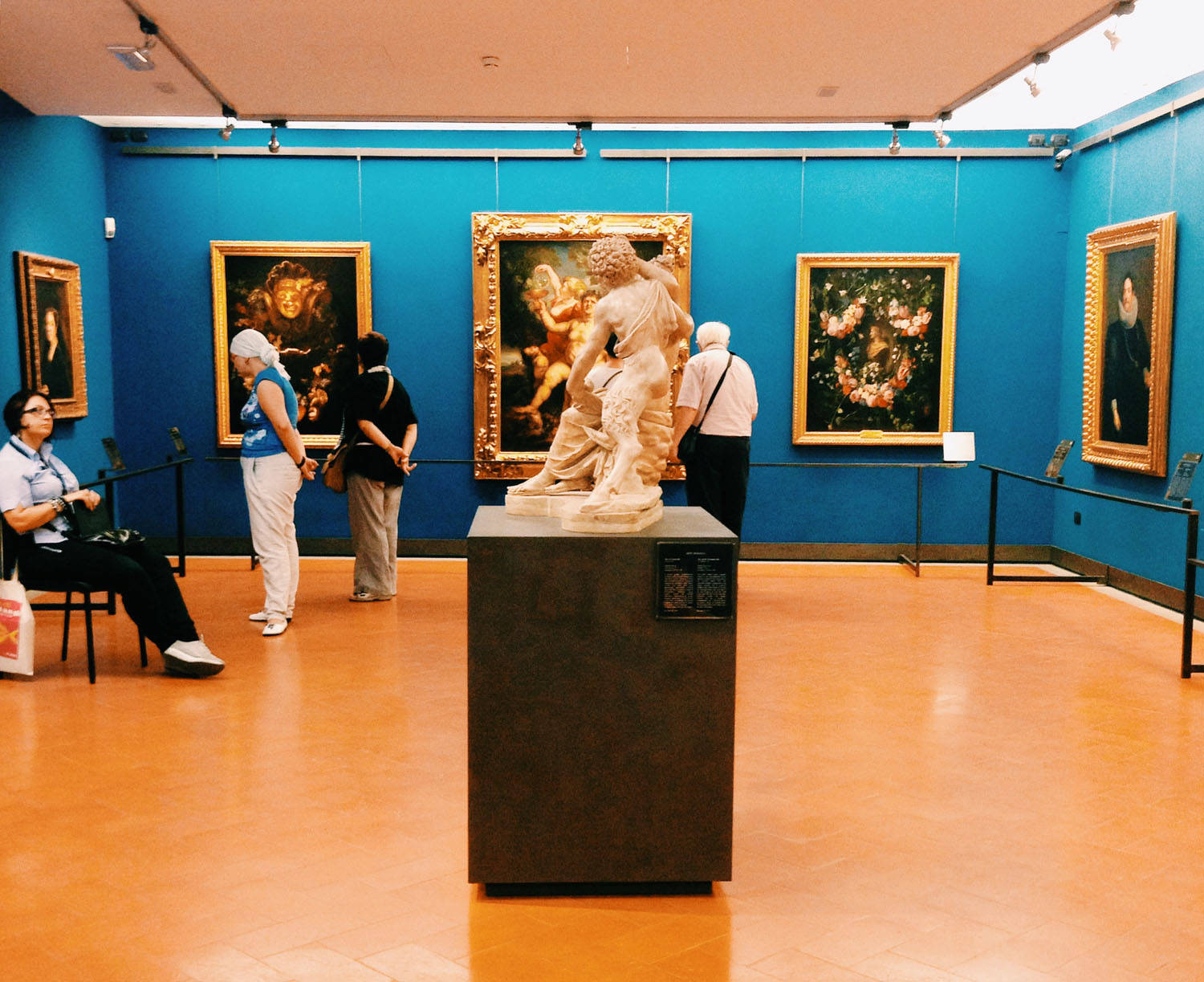 Museum 桌布 壁紙 — 訪客在擁有鮮豔藍色牆壁和溫暖陶土地板的博物館中欣賞古典雕塑和繪畫。