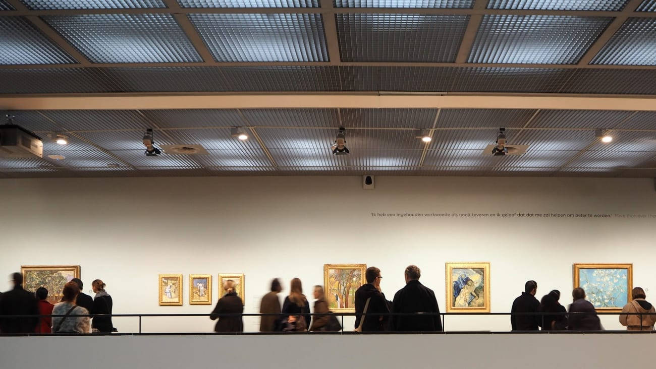 Museum 桌布 壁紙 — 訪客排隊觀看畫廊牆上帶框的畫作，天花板為網格設計並配有聚光燈。