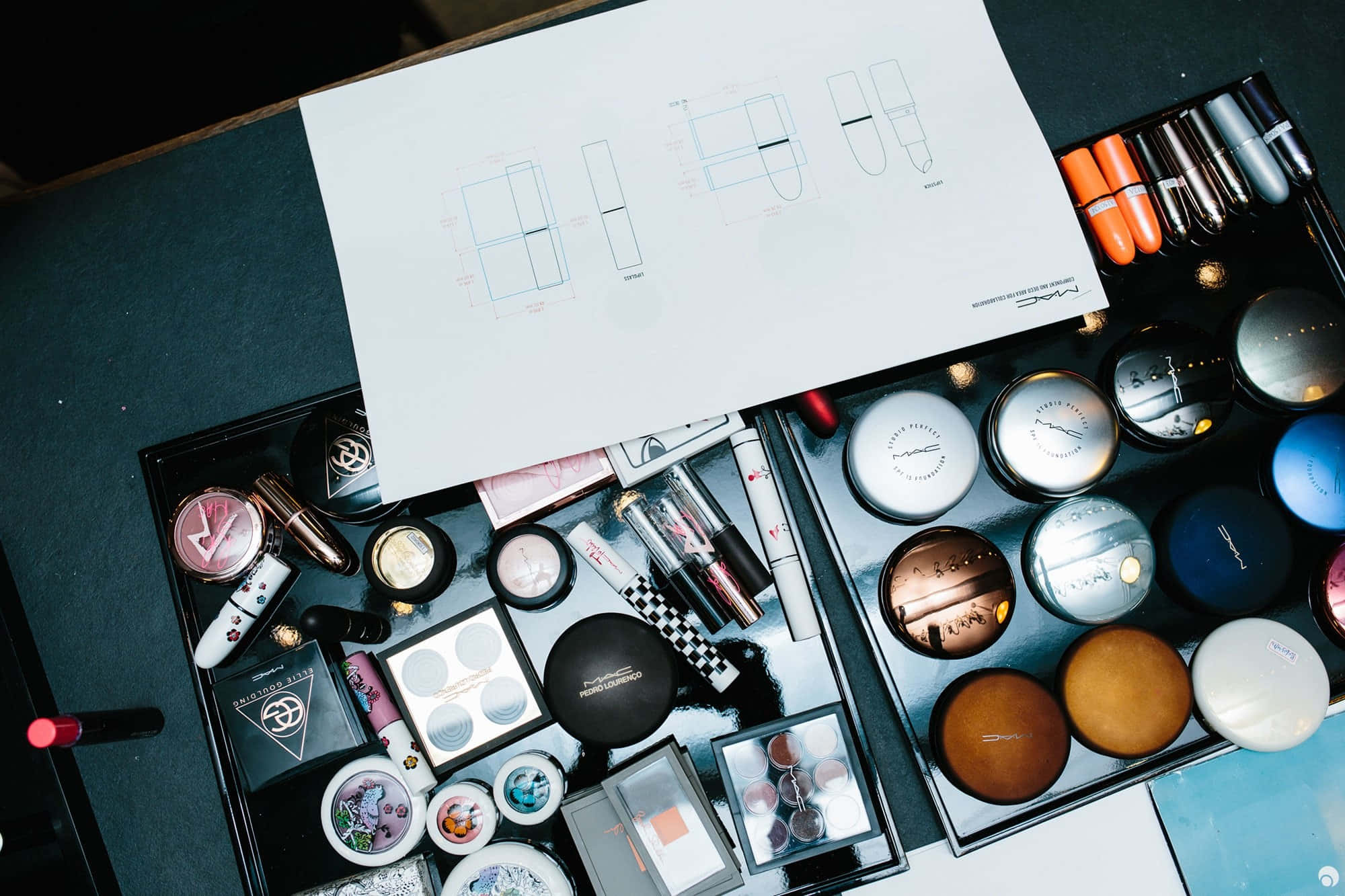 Mac Cosmetics 桌布 壁紙 — 設計師化妝台的俯視圖，散落著化妝品和產品包裝的技術圖紙。