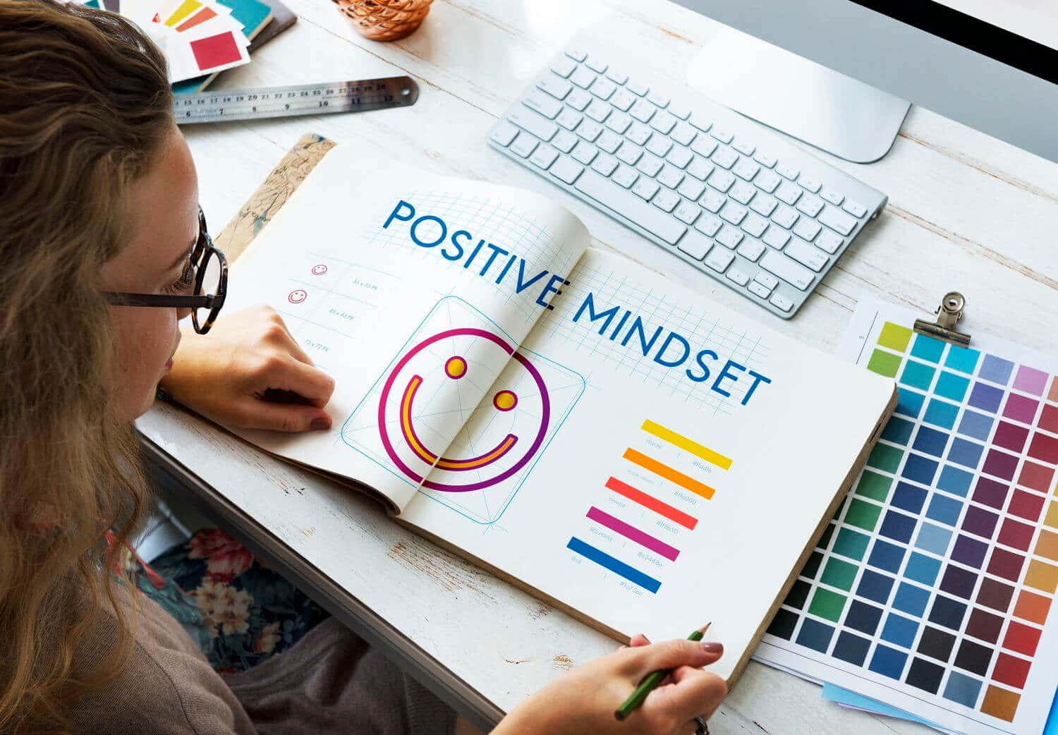 Journaling 桌布 壁紙 — 設計師在名為「Positive Mindset」的筆記本上草繪一個色彩繽紛的笑臉，周圍環繞著色板和鍵盤。
