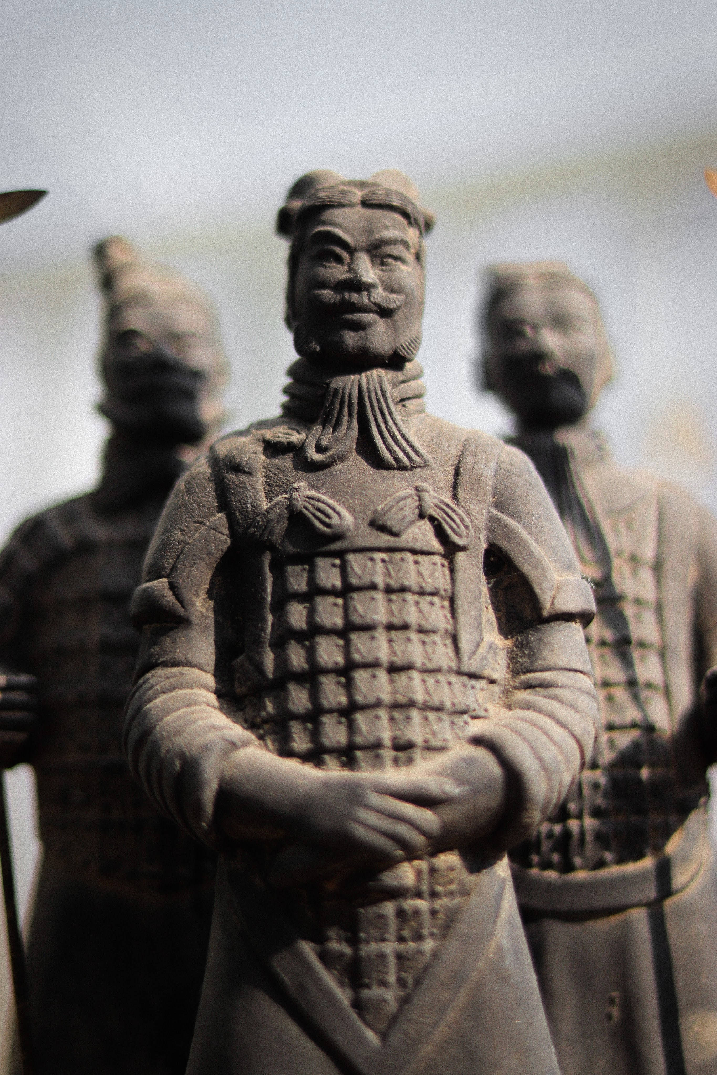 Warrior 桌布 壁紙 — 詳細的兵馬俑雕像特寫，具有複雜的盔甲和寧靜的表情，周圍是模糊的同伴士兵。