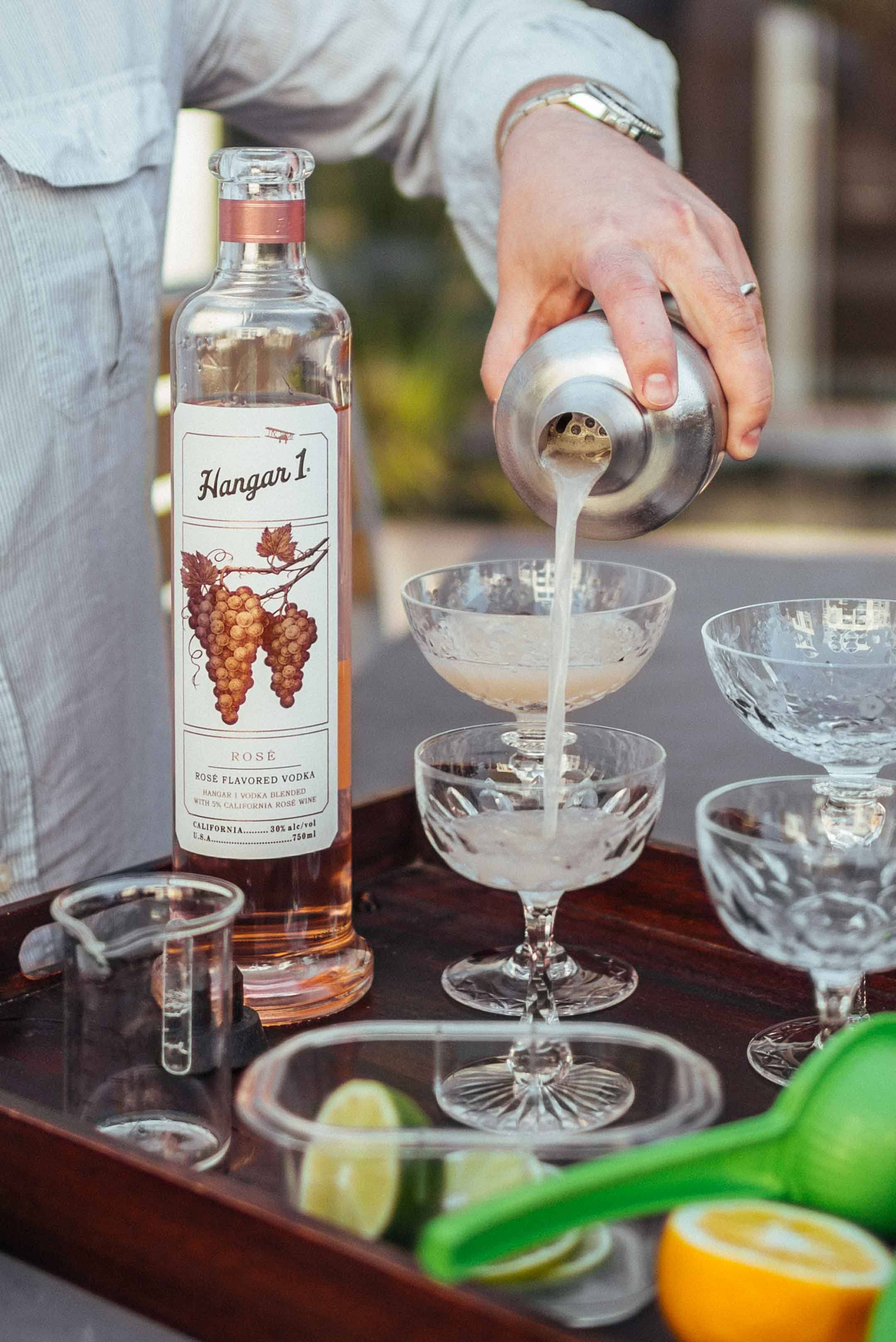 cocktail 桌布 壁紙 — 調酒師將玫瑰味伏特加從銀色搖酒壺倒入木托盤上的水晶杯，配以柑橘裝飾。
