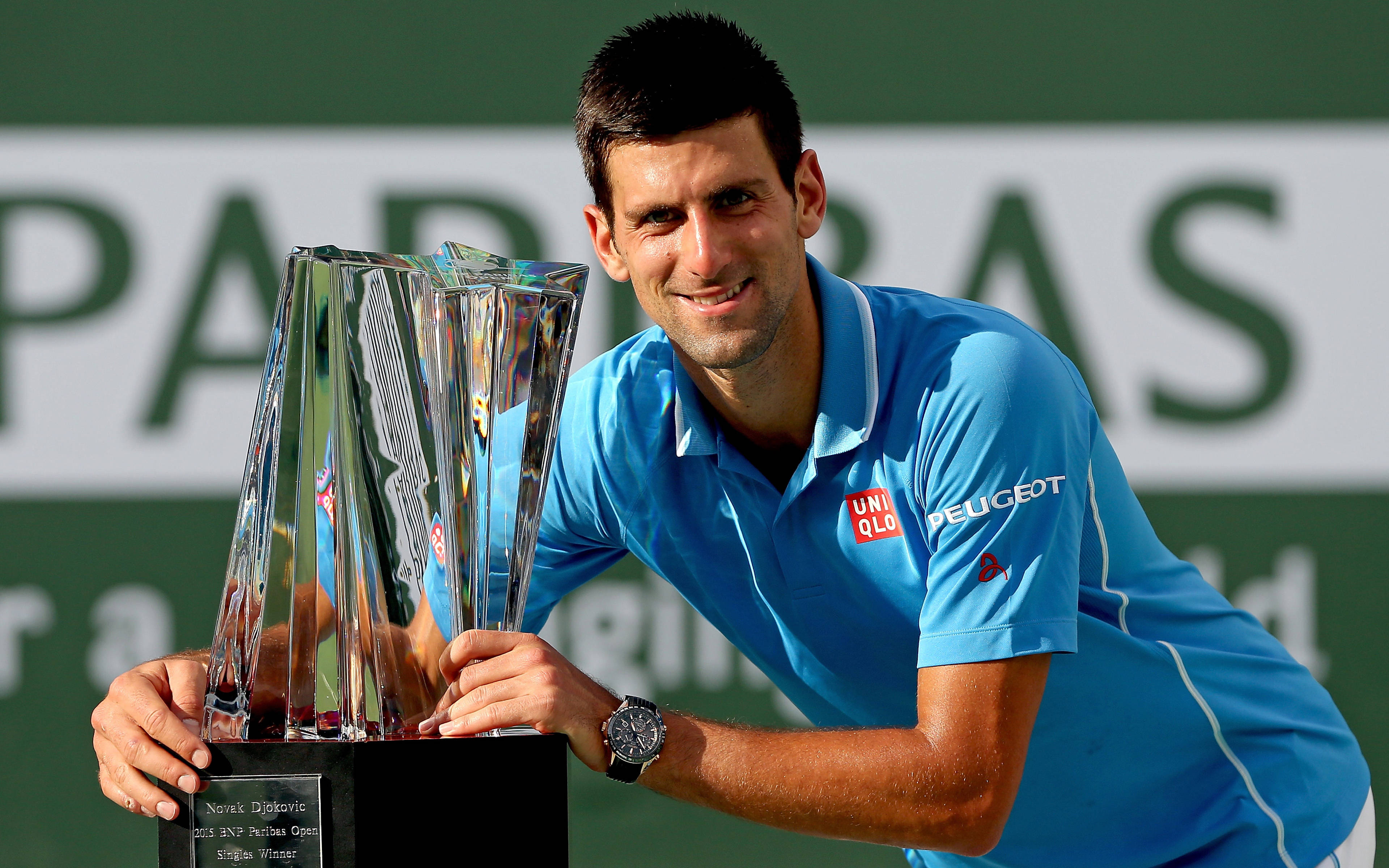 Novak 桌布 壁紙 — 諾瓦克·喬科維奇在綠色球場上自豪地微笑，手持一個大型水晶網球獎盃。