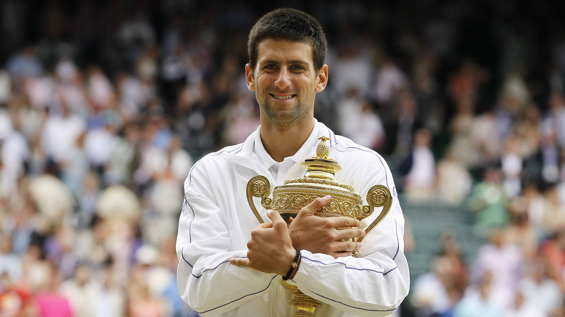 Novak 桌布 壁紙 — 諾瓦克·喬科維奇自豪地微笑，手持溫布頓獎盃，背景是模糊的人群。