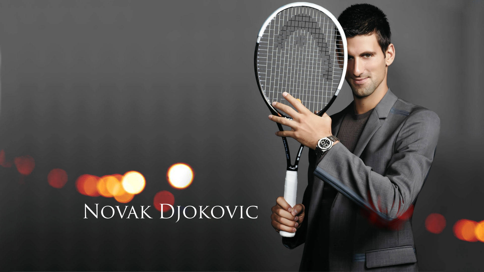Novak 桌布 壁紙 — 諾瓦克·喬科維奇身穿灰色西裝，在黑暗背景下手持網球拍，背景有溫暖的散景燈光。