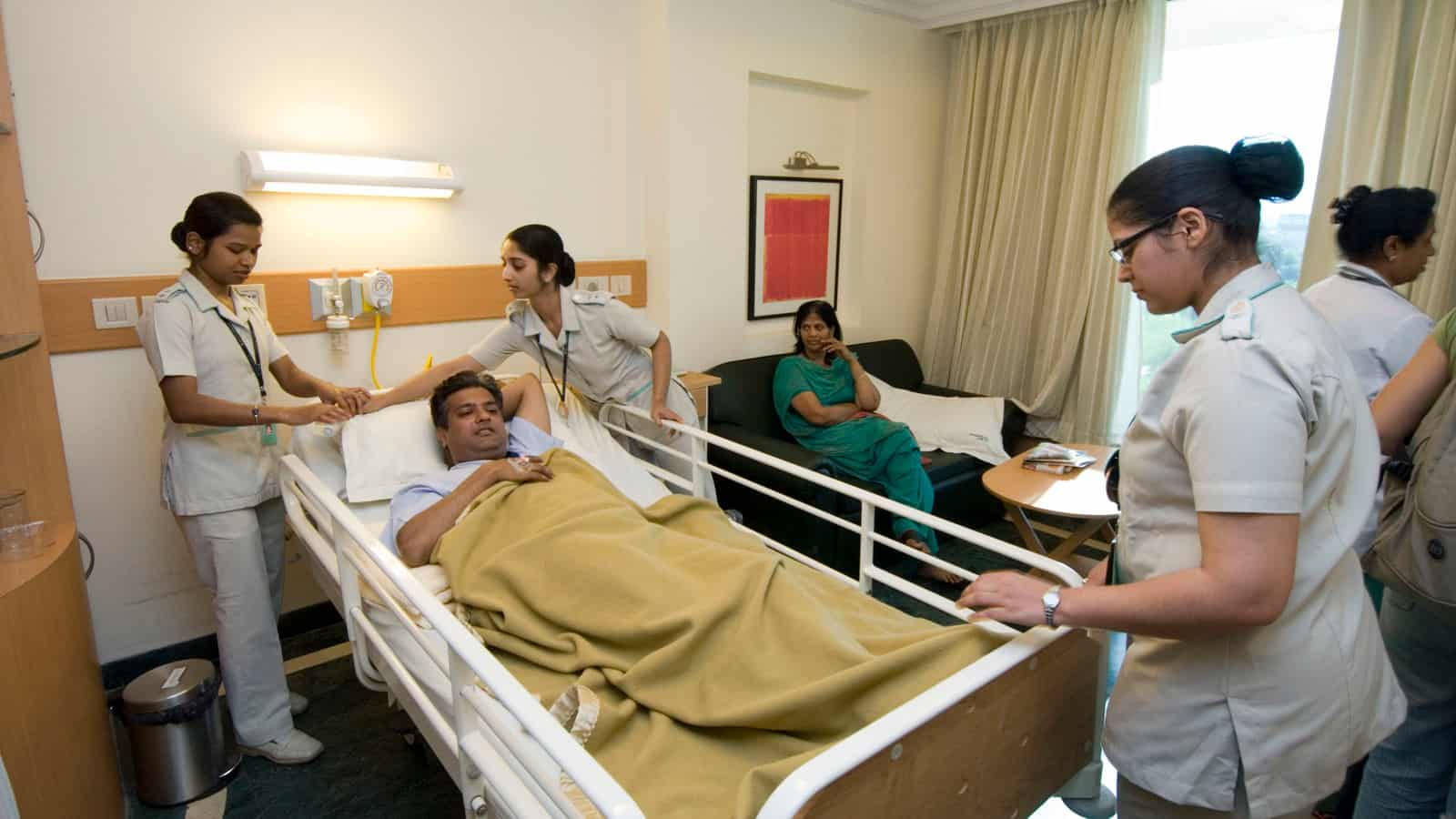 Nurse 桌布 壁紙 — 護士在醫院病床上照顧病人，而訪客則坐在附近安靜的房間裡。