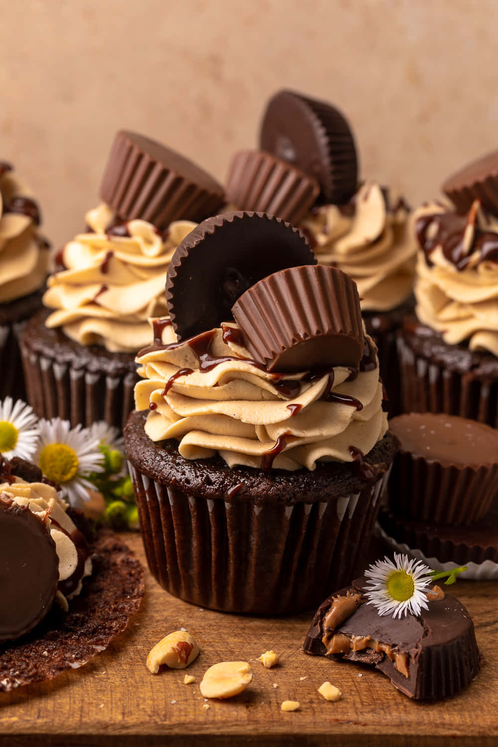 Cupcake 桌布 壁紙 — 豐富的巧克力紙杯蛋糕，上面有花生醬糖霜和Reese's杯，放在木板上，配以雛菊和散落的花生。