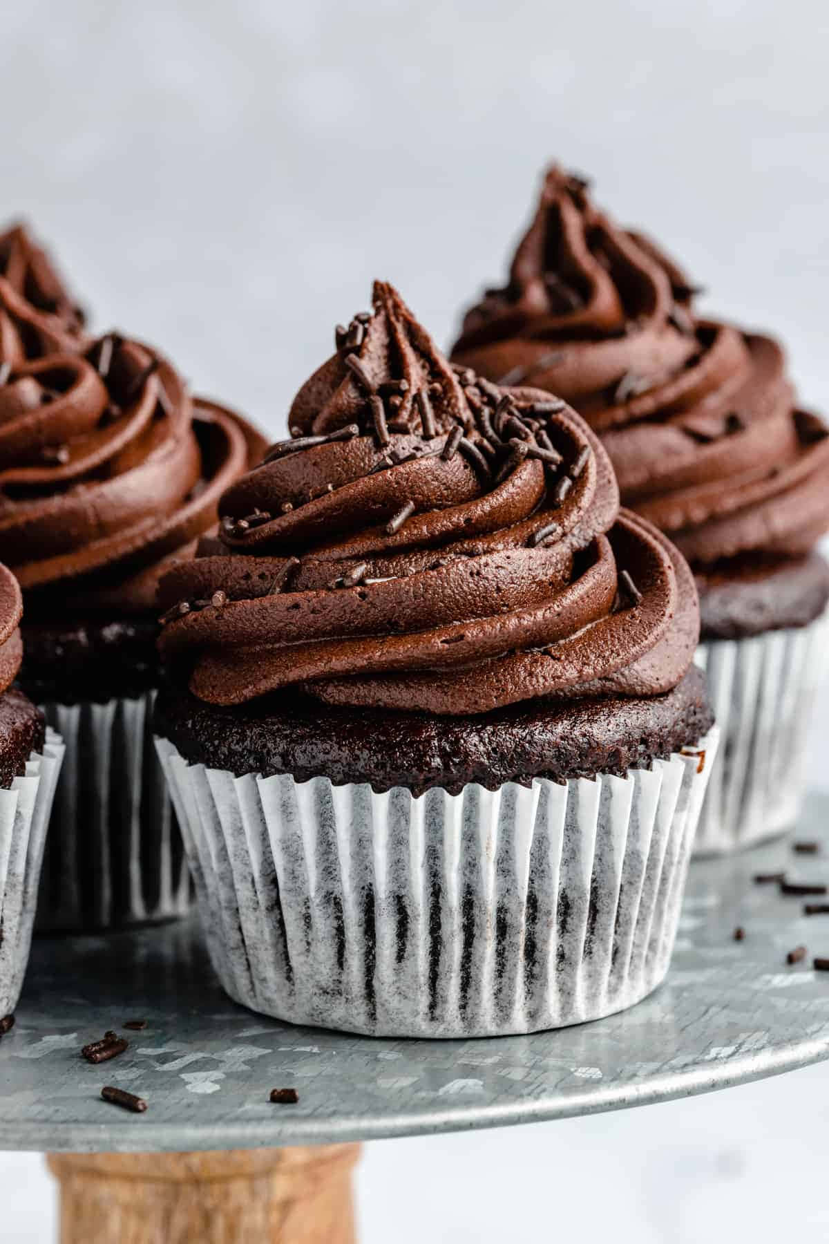 Cupcake 桌布 壁紙 — 豐富的巧克力紙杯蛋糕，帶有光澤的漩渦和糖粒，放在一個質樸的金屬架上，背景是柔和的灰色。