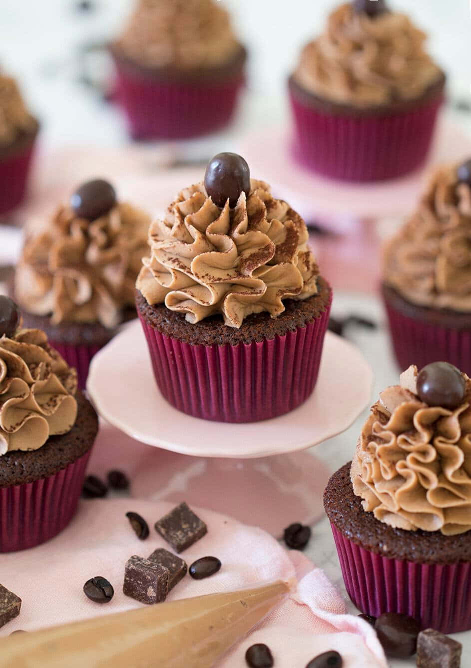 Cupcake 桌布 壁紙 — 豐富的巧克力紙杯蛋糕配咖啡奶油霜和巧克力裝飾，擺放在粉紅色架和布上。