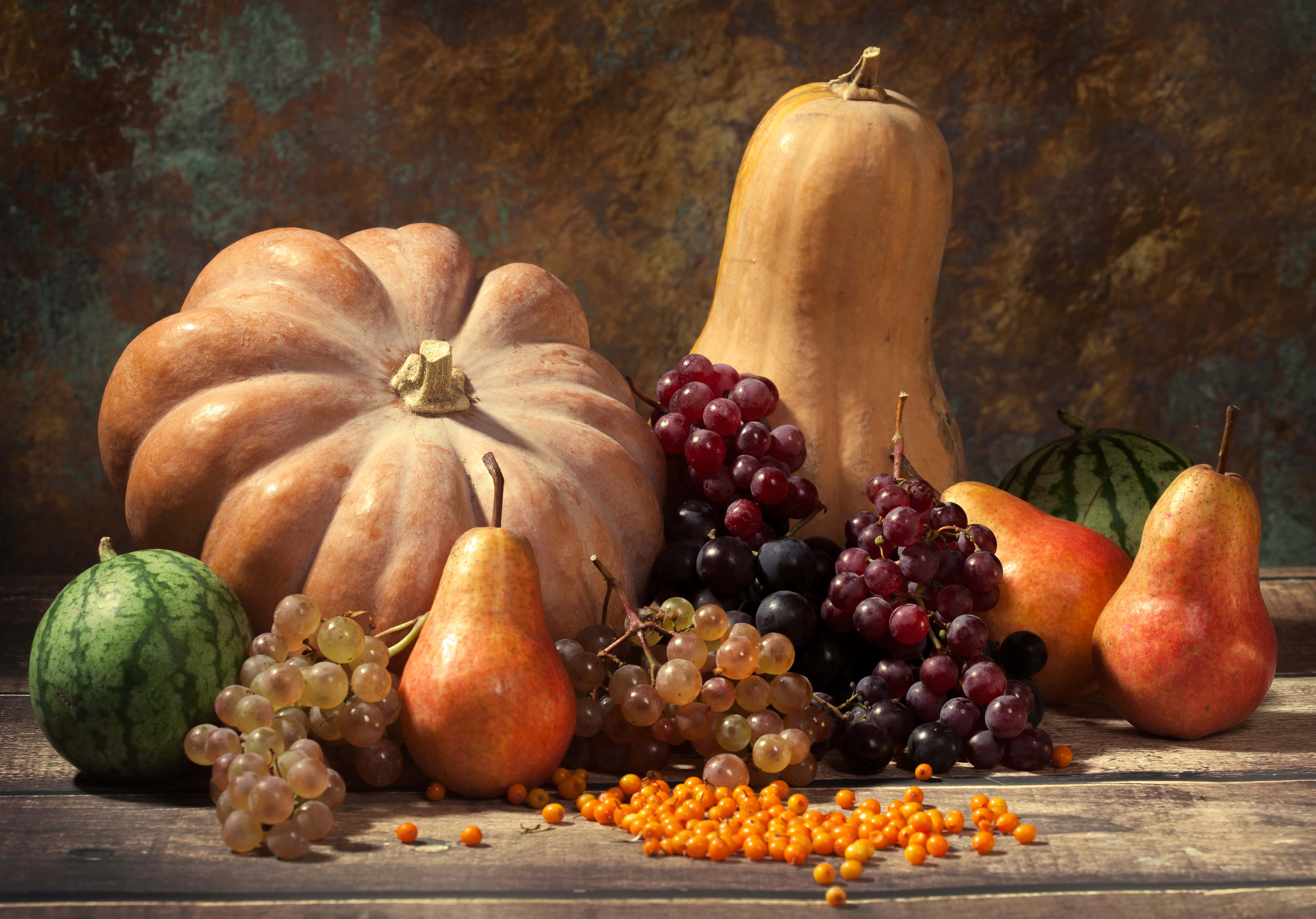 Autumn Food 桌布 壁紙 — 豐富的秋日靜物畫，南瓜、梨、葡萄和西瓜擺放在質樸的木桌上，背景帶有紋理。